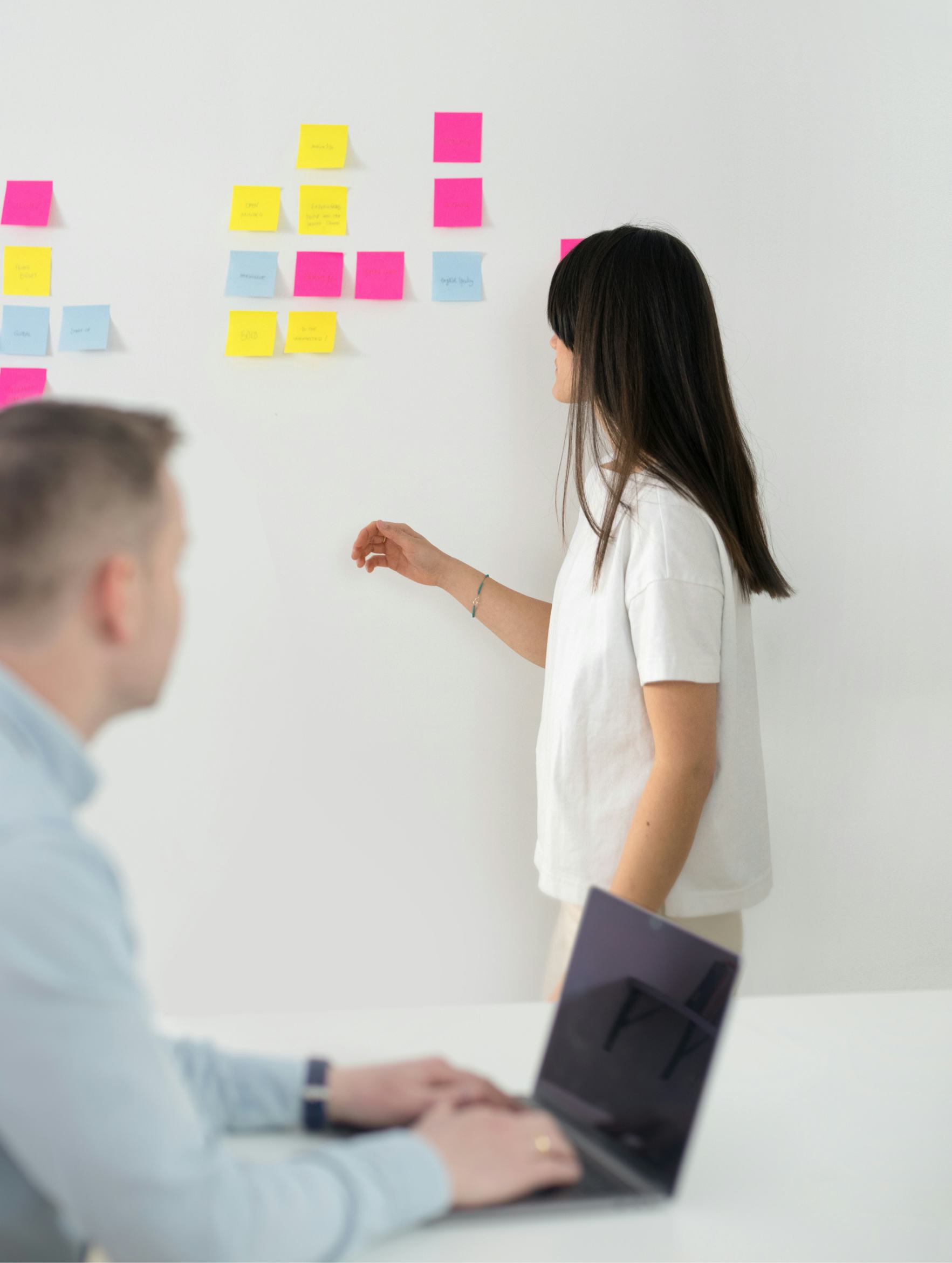 Photo of Sarah organizing post-its on a whiteboard while Hjörtur is on his laptop