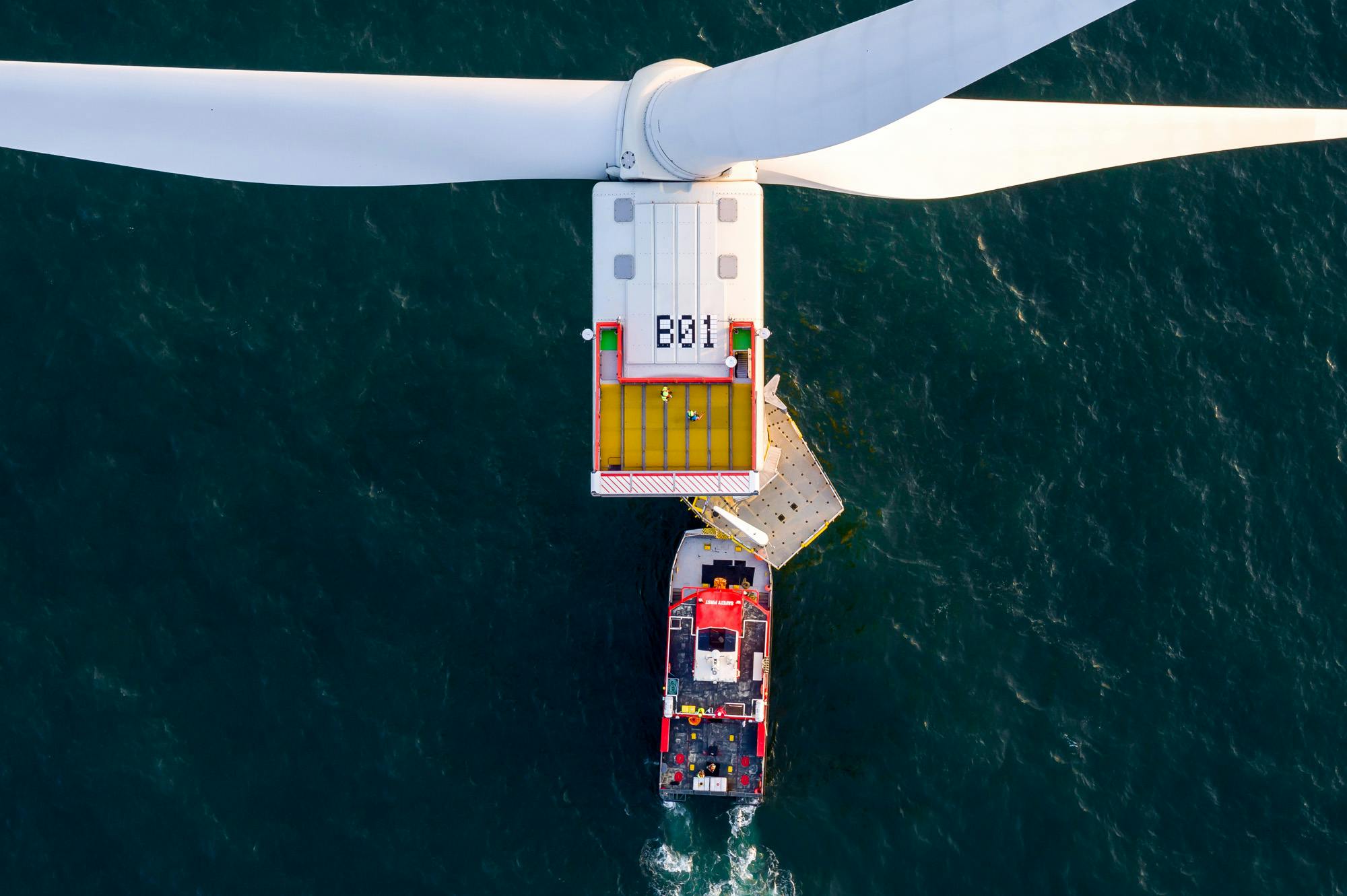 An aerial view of a boat approach a wind turbine in the ocean