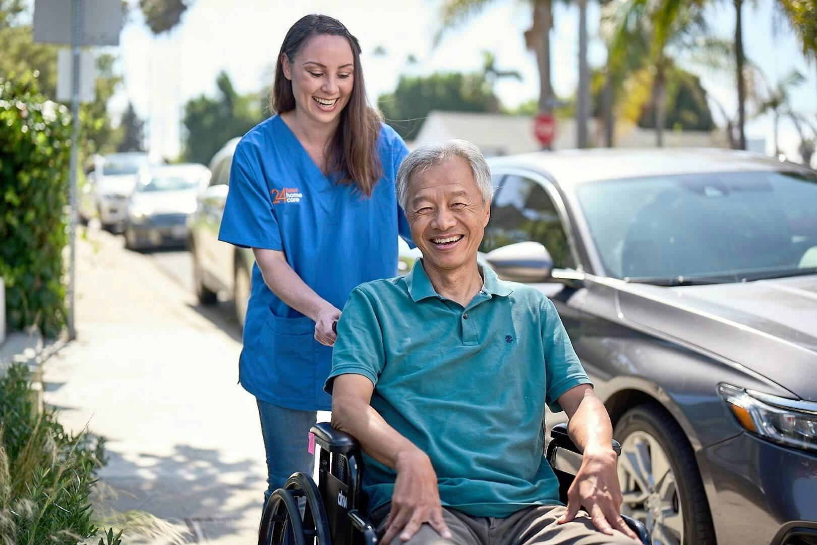 An adult female caregiver pushes an elderly client down the street in his wheelchair.