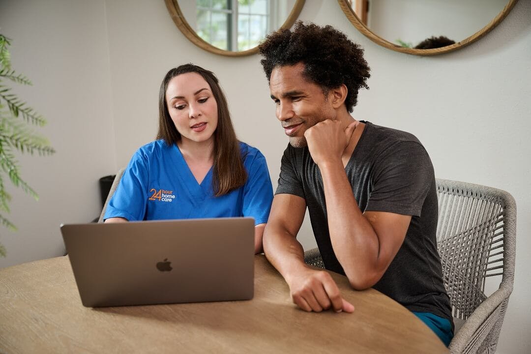 A female caregiver and an adult client review contracts on a laptop.