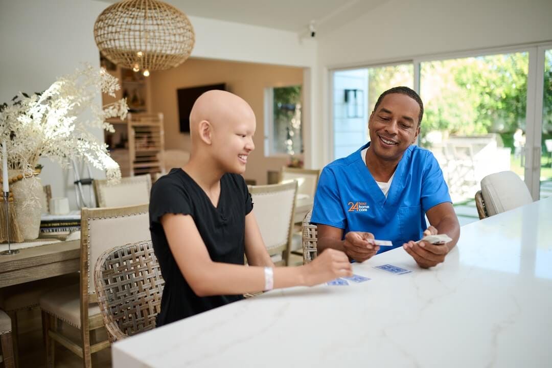 A 24 Hour Home Care caregiver plays cards at the kitchen counter with his child client.