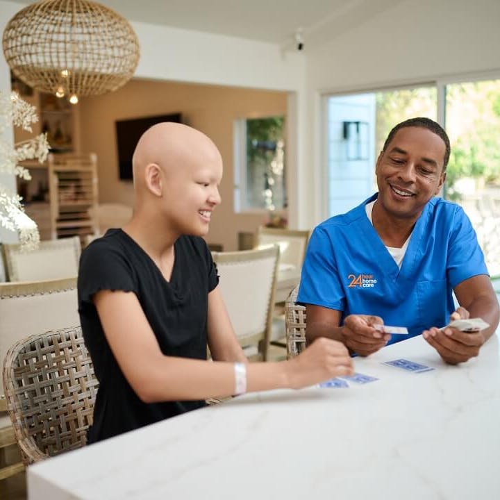A 24 Hour Home Care caregiver plays cards at the kitchen counter with his child client.