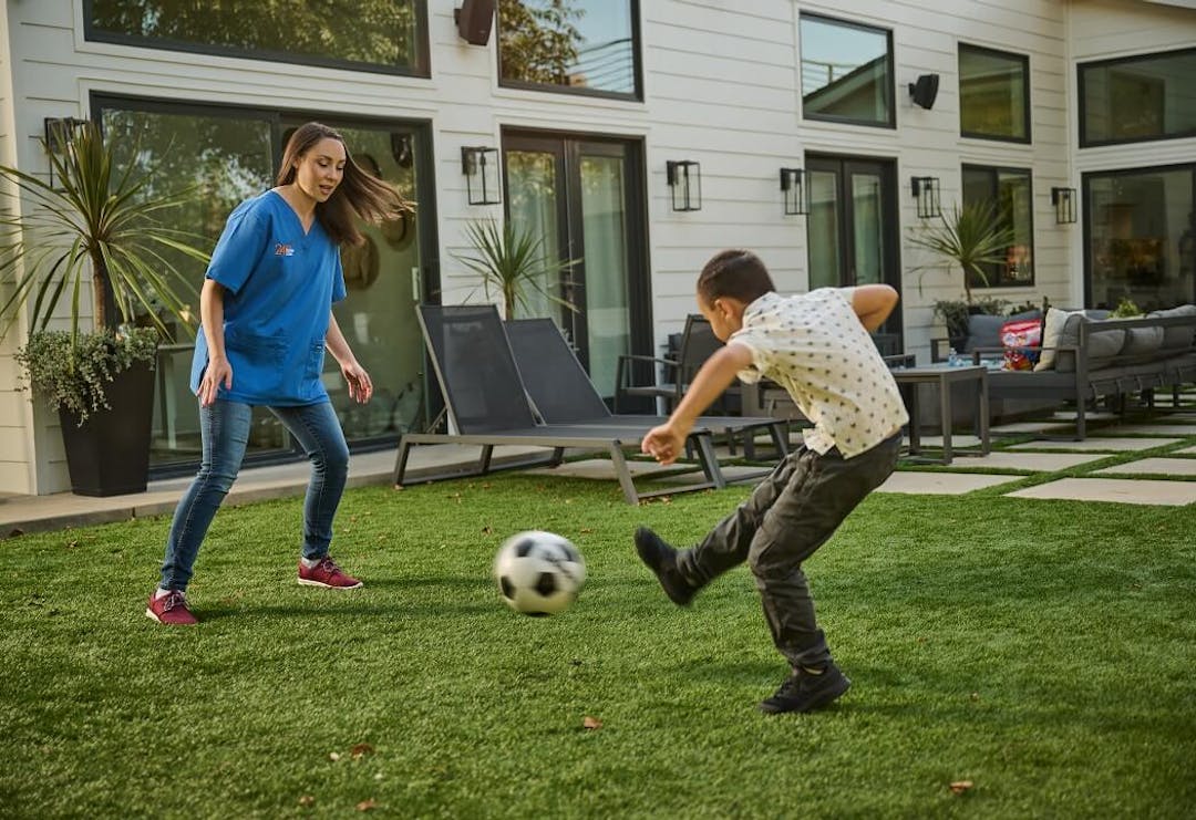A social recreation coach plays soccer outside with her young client.
