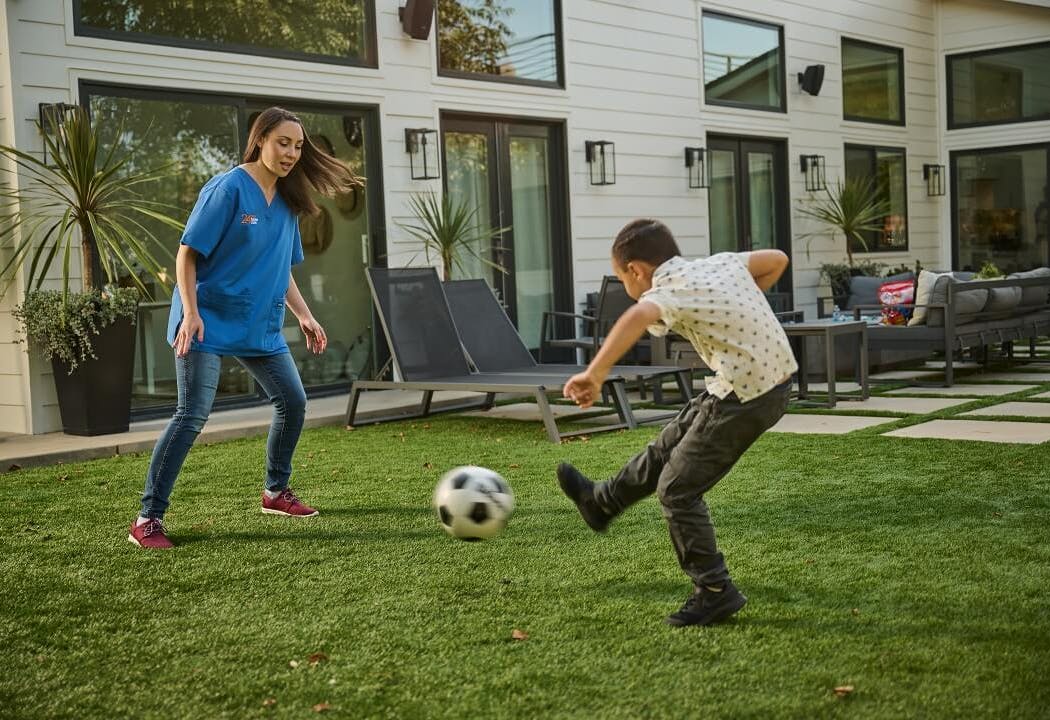 A social recreation coach plays soccer outside with her young client.