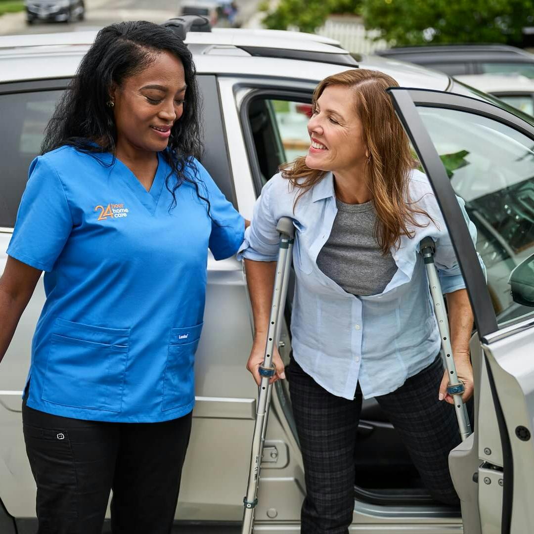 A 24 Hour Home Care caregiver helps her client on crutches out of the car.