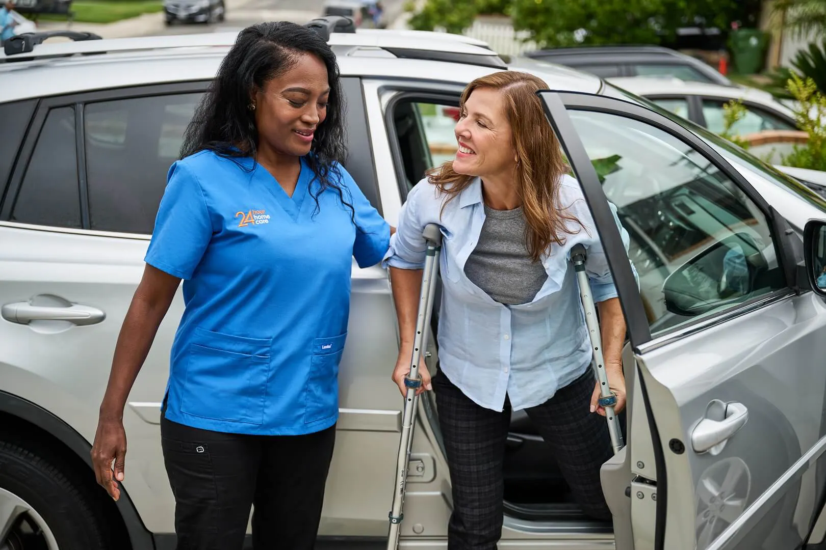 A 24 Hour Home Care caregiver helps her client on crutches out of the car.
