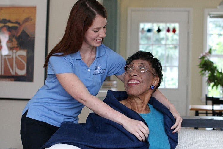 caregiver-exchanging-smiles-with-woman-while-wrapping-blanket-around-her