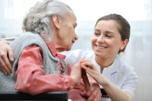 A woman smiles at an elderly woman in a chair