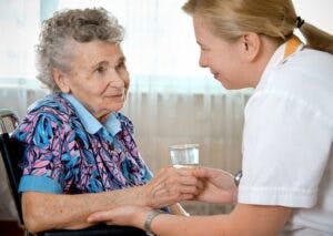 A woman helping an elderly woman by holding her arm and a drink