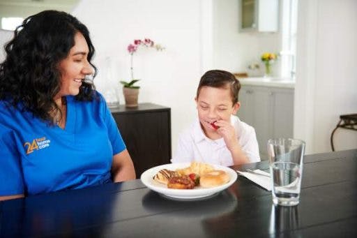 A child with disabilities and his care provider eat lunch together.