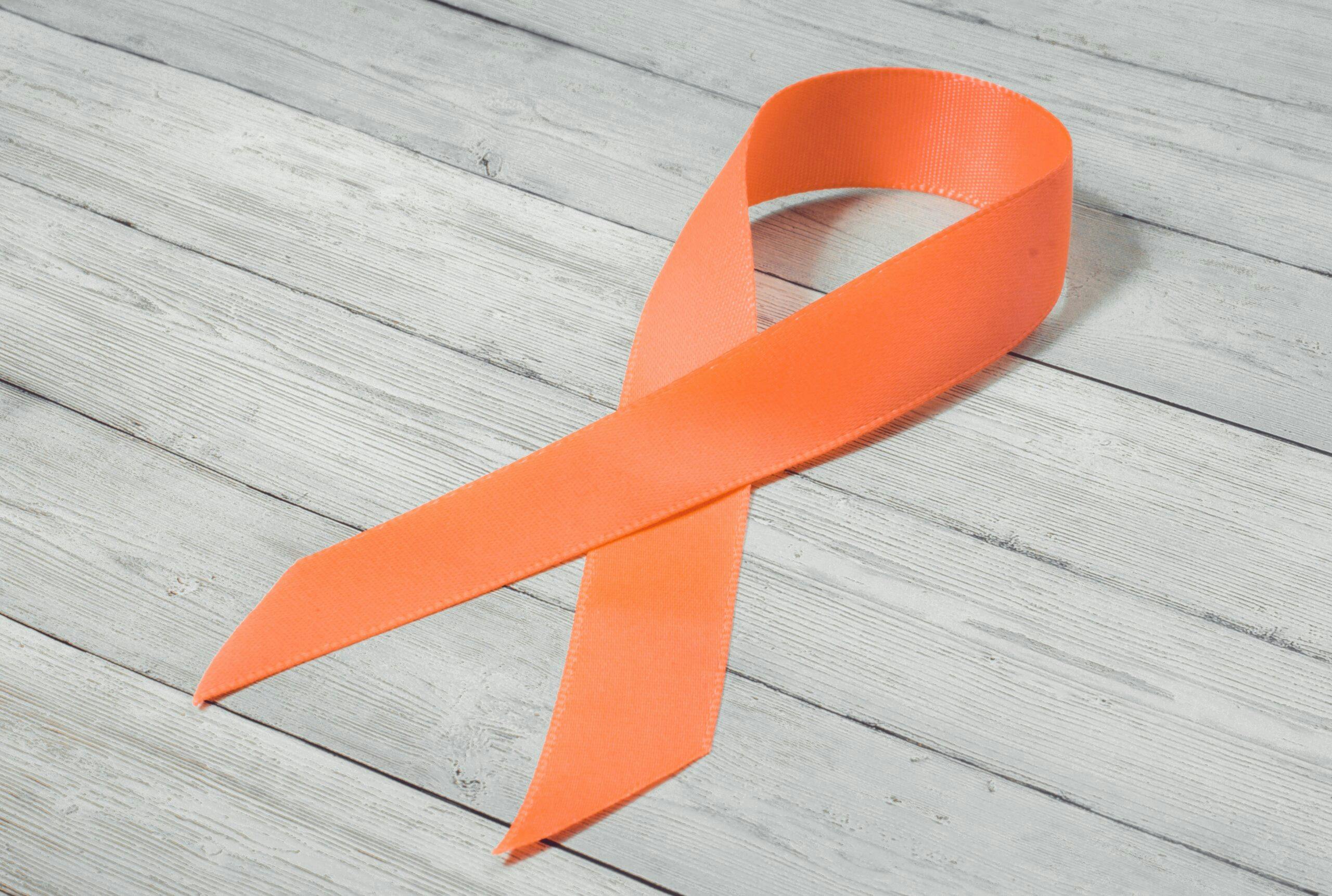 Orange ribbon on wooden background, symbol of the problem of violence against women, kidney cancer association, symbol of solidarity