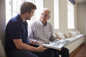 An elderly man looks at a photo book with another man on a bench