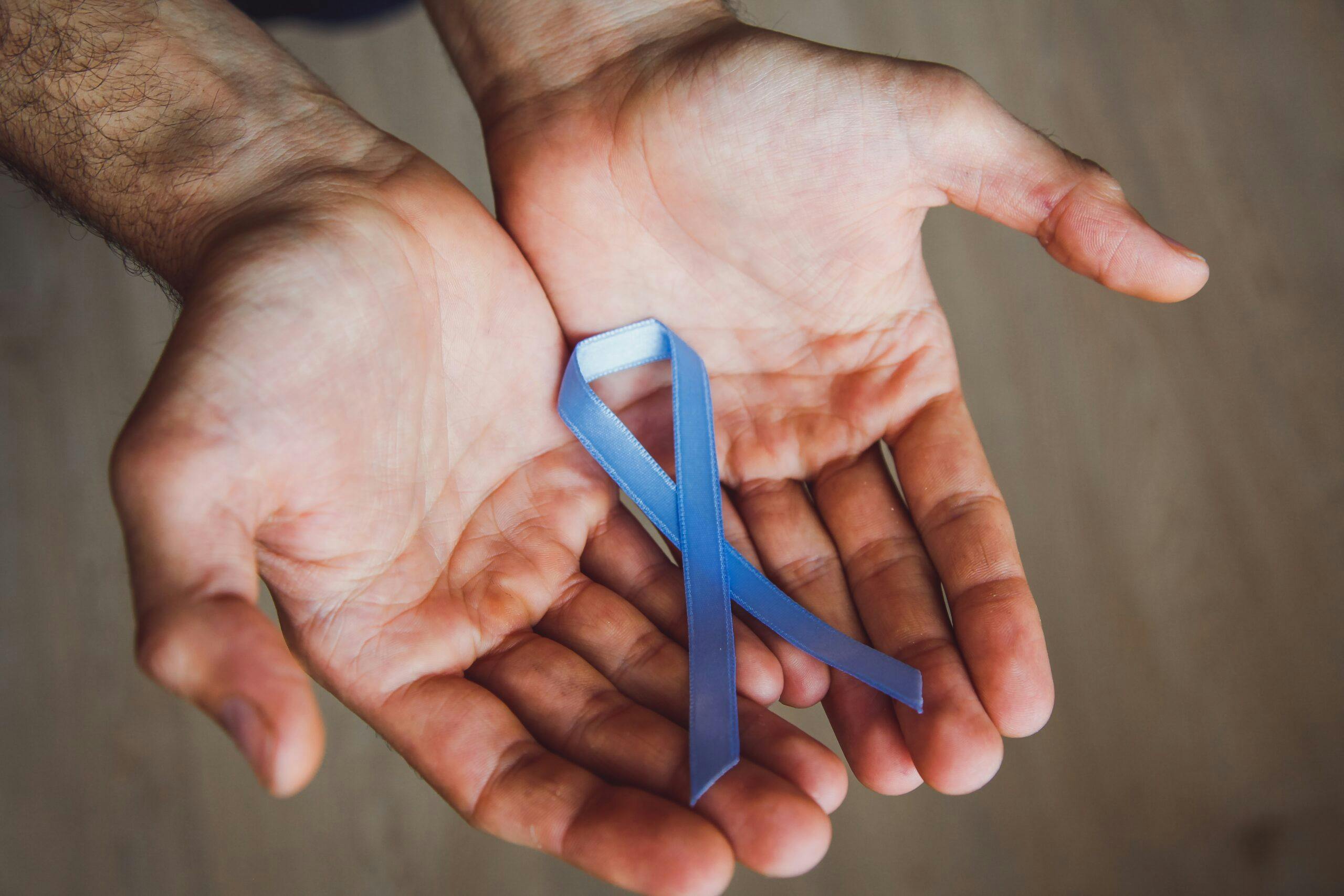 mans-hand-holding-a-blue-ribbon-simbol-of-prostate-cancer-awareness-month-mens-cancer-concept_t20_KvWZwx