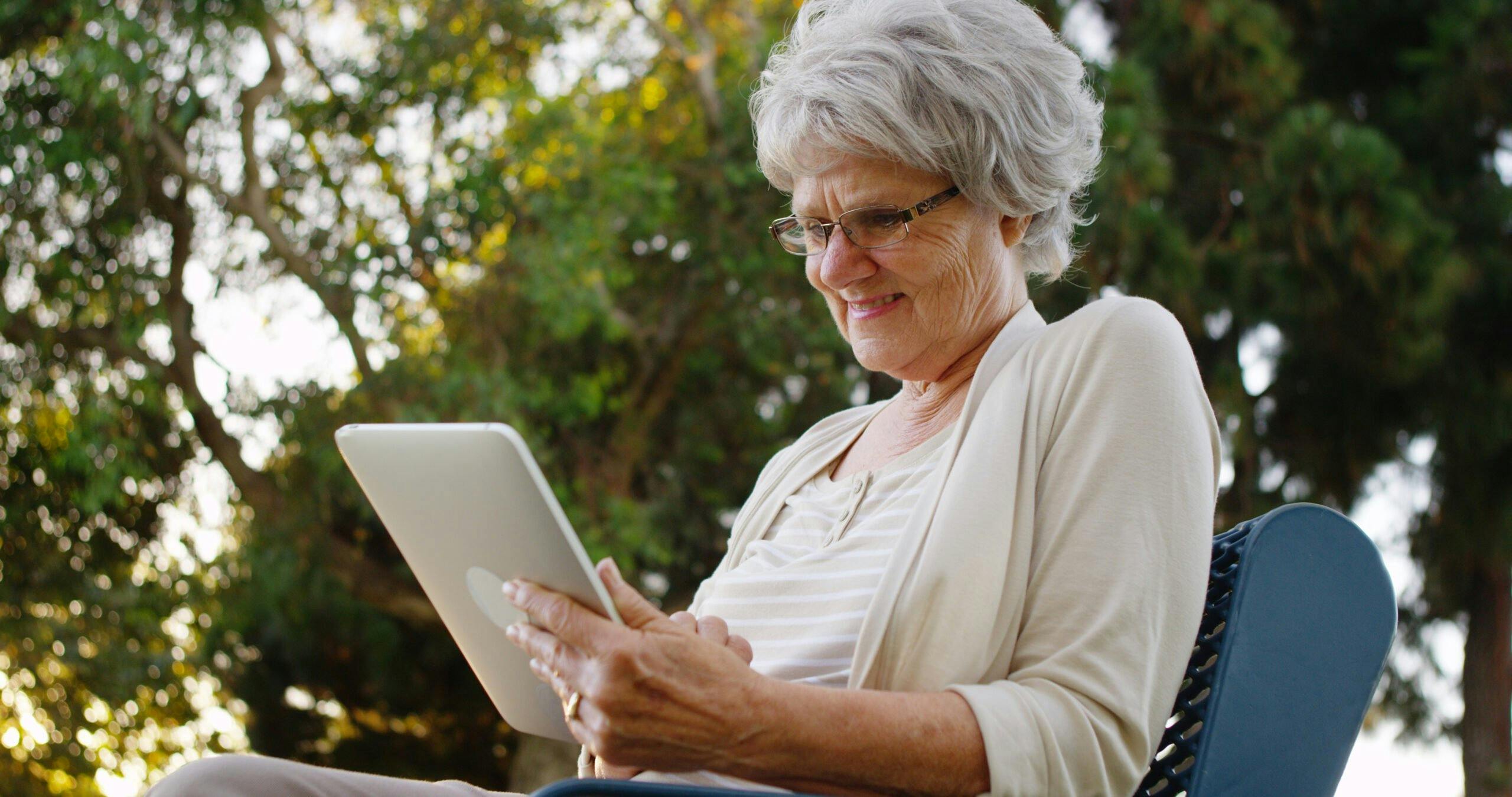 Happy senior woman using tablet at the park