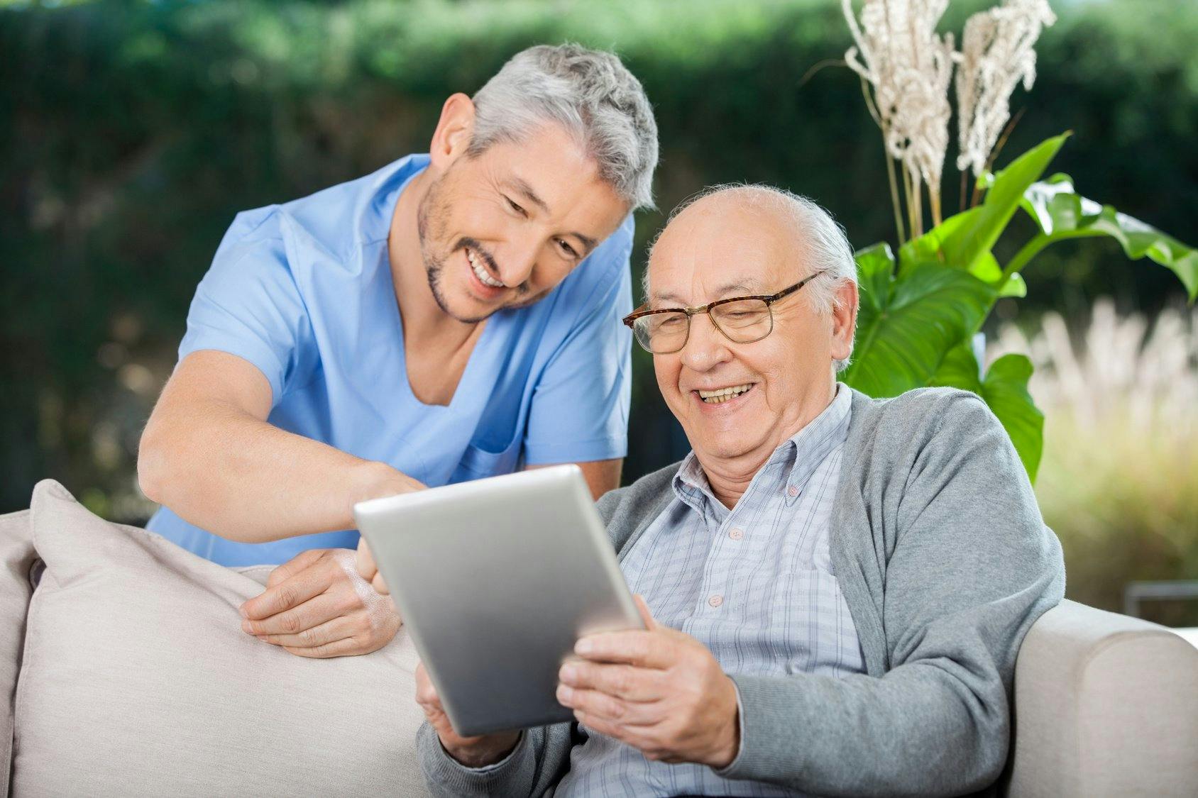 Happy Caretaker And Senior Man Using Tablet PC