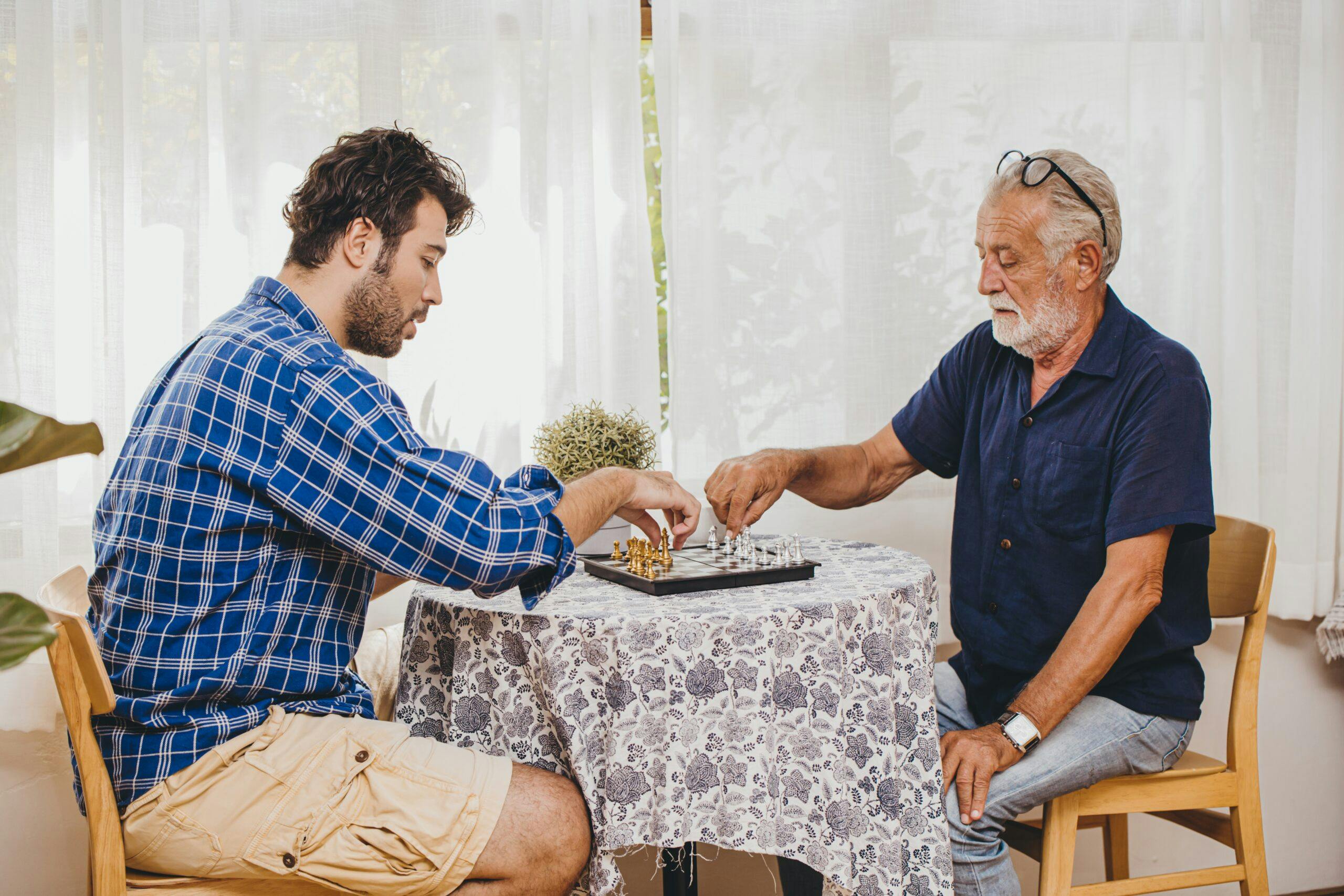 Smart old man playing chess board game with his son at home.
