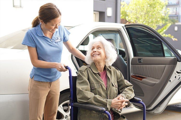 caregiver_helps_elderly_woman_in_wheelchair_from_car