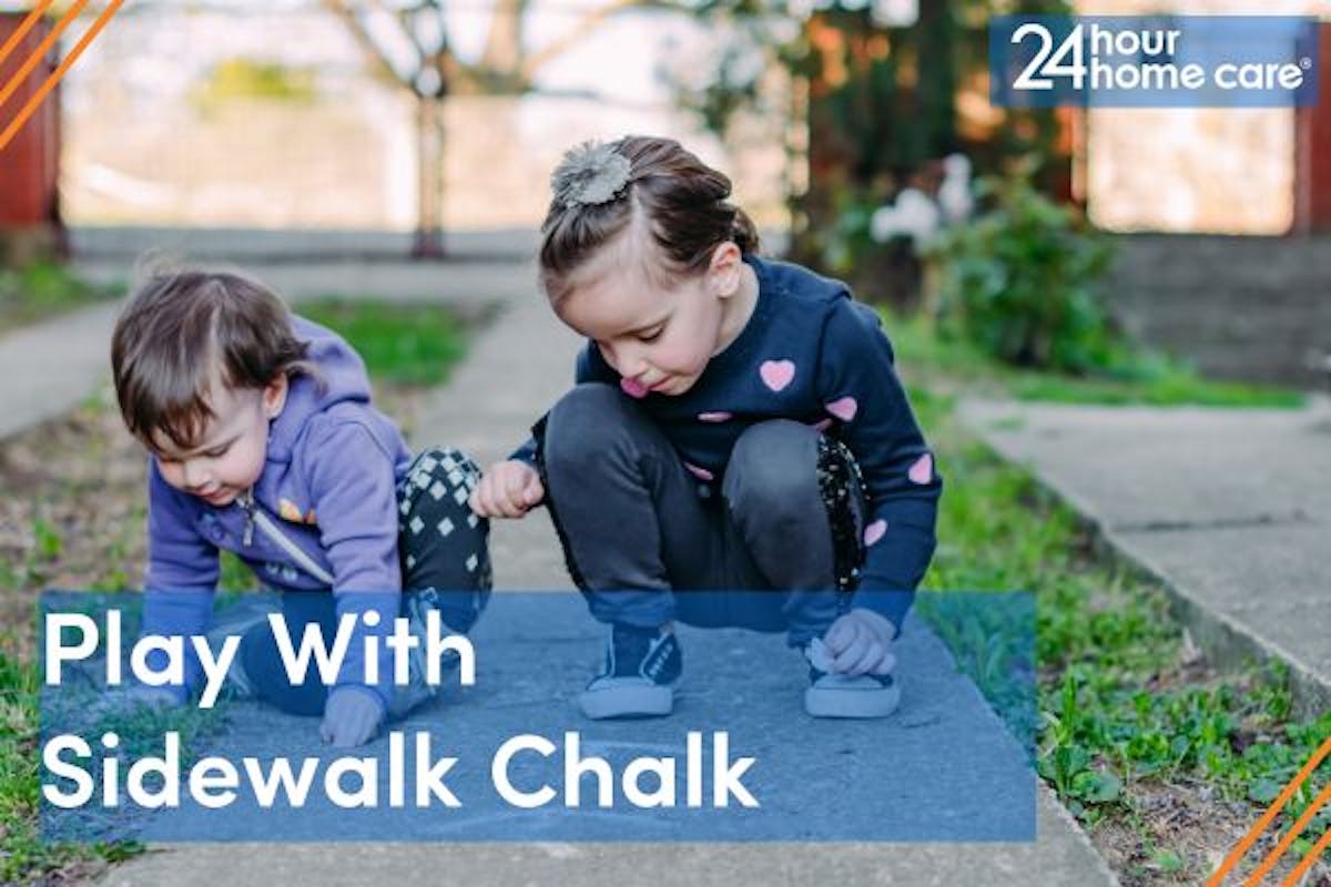 Two children play outside with sidewalk chalk.