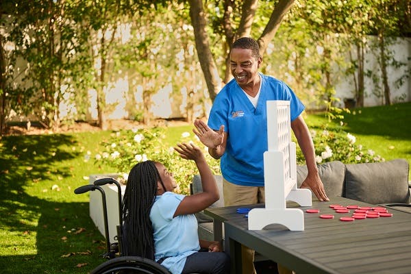 A caregiver plays connect 4 outside with a child with a disability.
