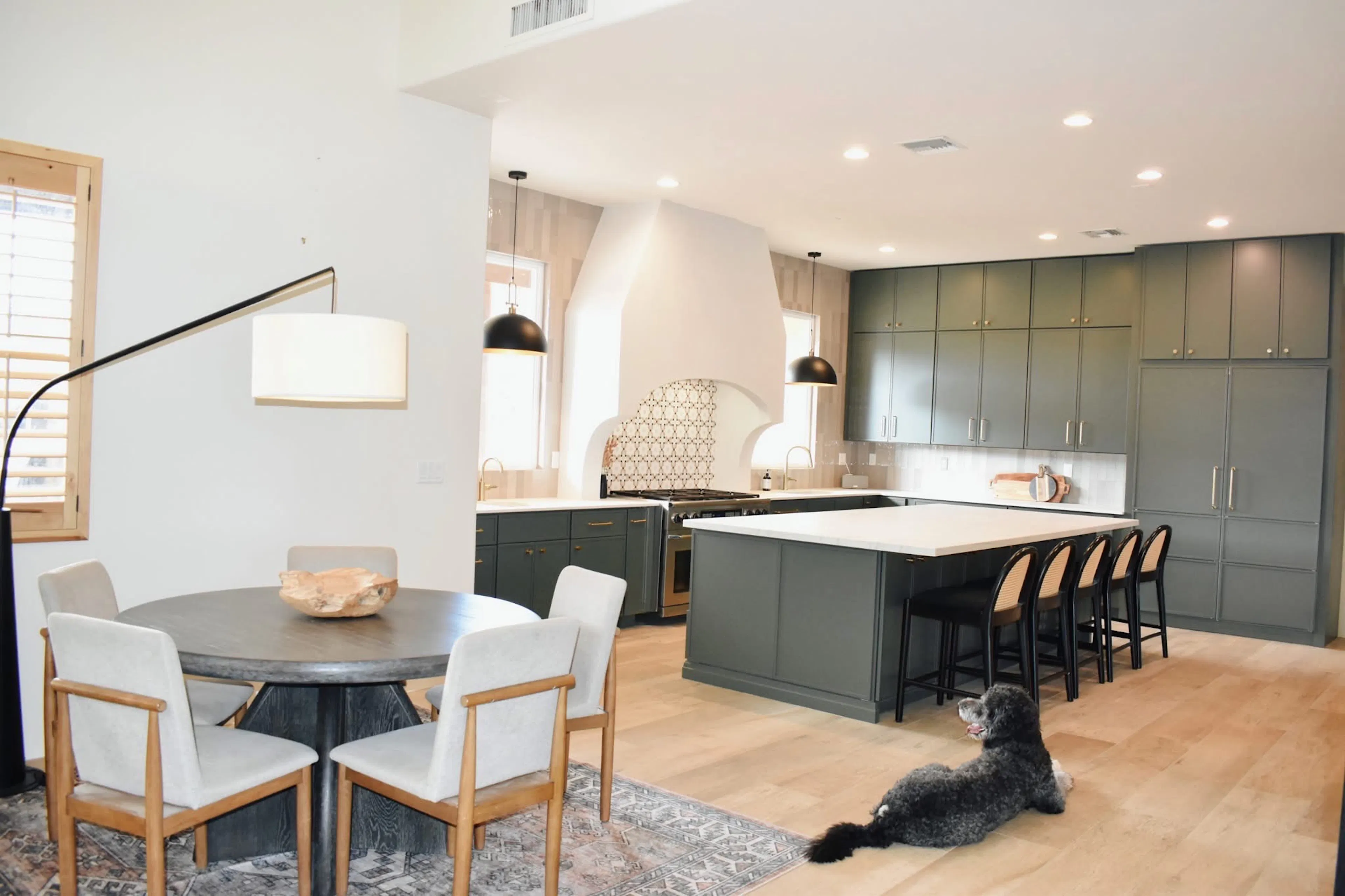 Open dining area looking into a remodeled green kitchen with a large island and custom storage.