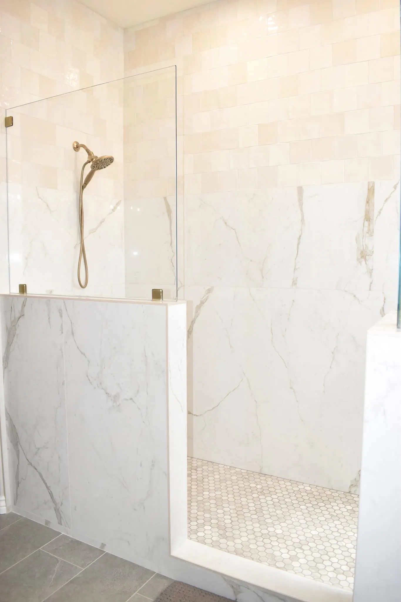 Open shower entry finished with marble-look wall panels, glossy tile, brass fixtures, and mosaic flooring.