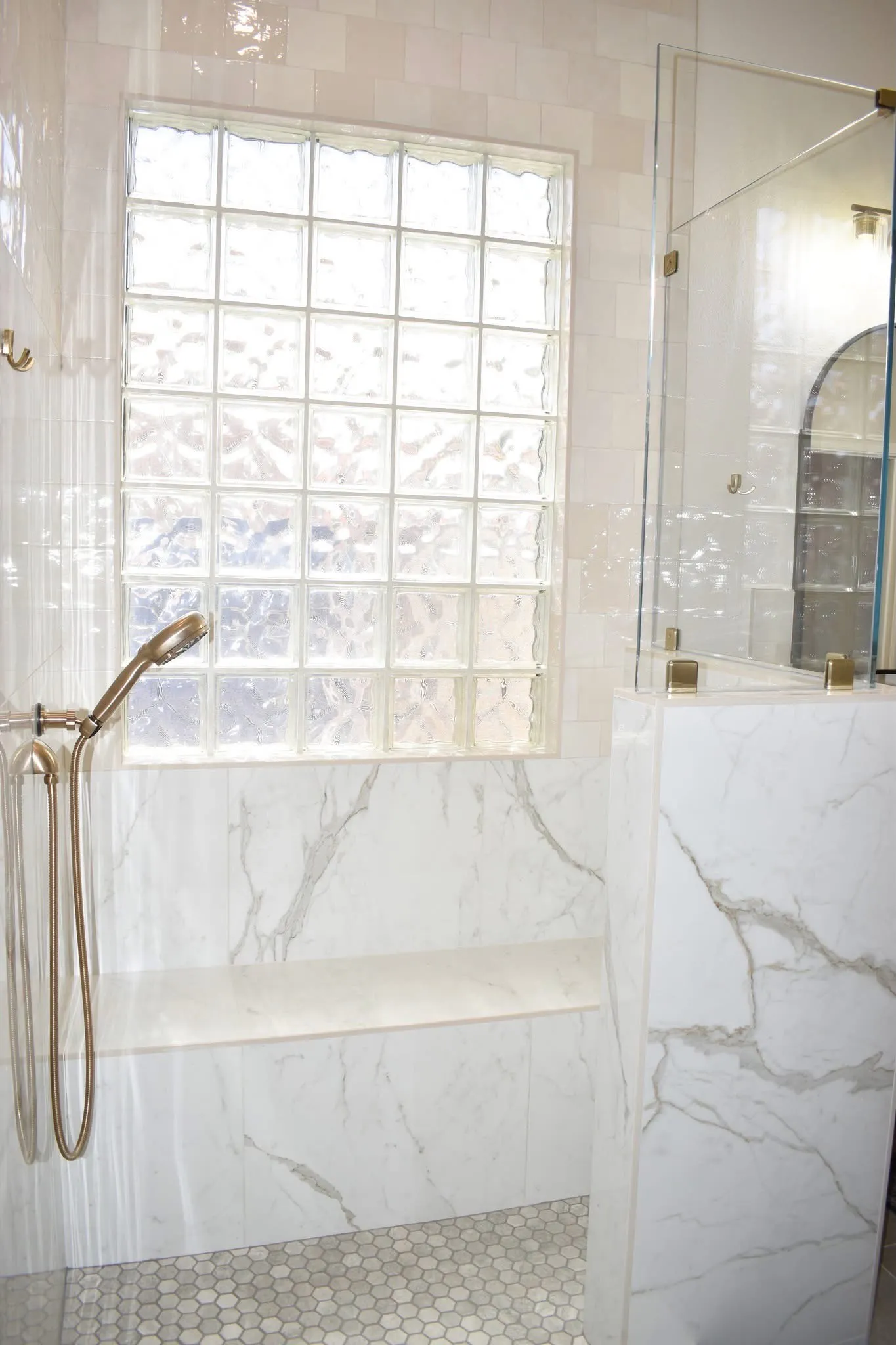 Light wood double vanity with white countertop, arched black mirrors, brass fixtures, and adjacent glass shower.