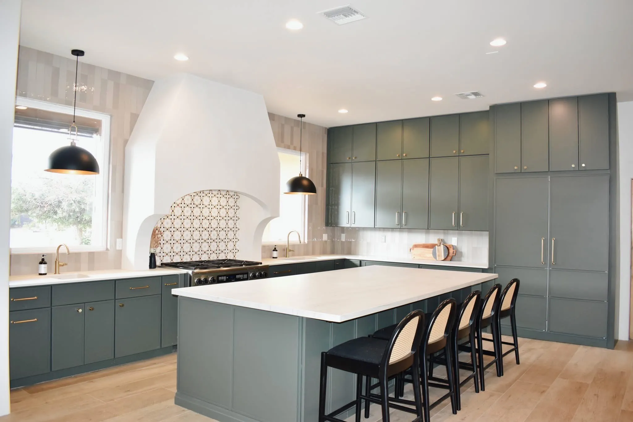 Remodeled kitchen with green cabinetry, a large white island, brass fixtures, and black pendant lights.