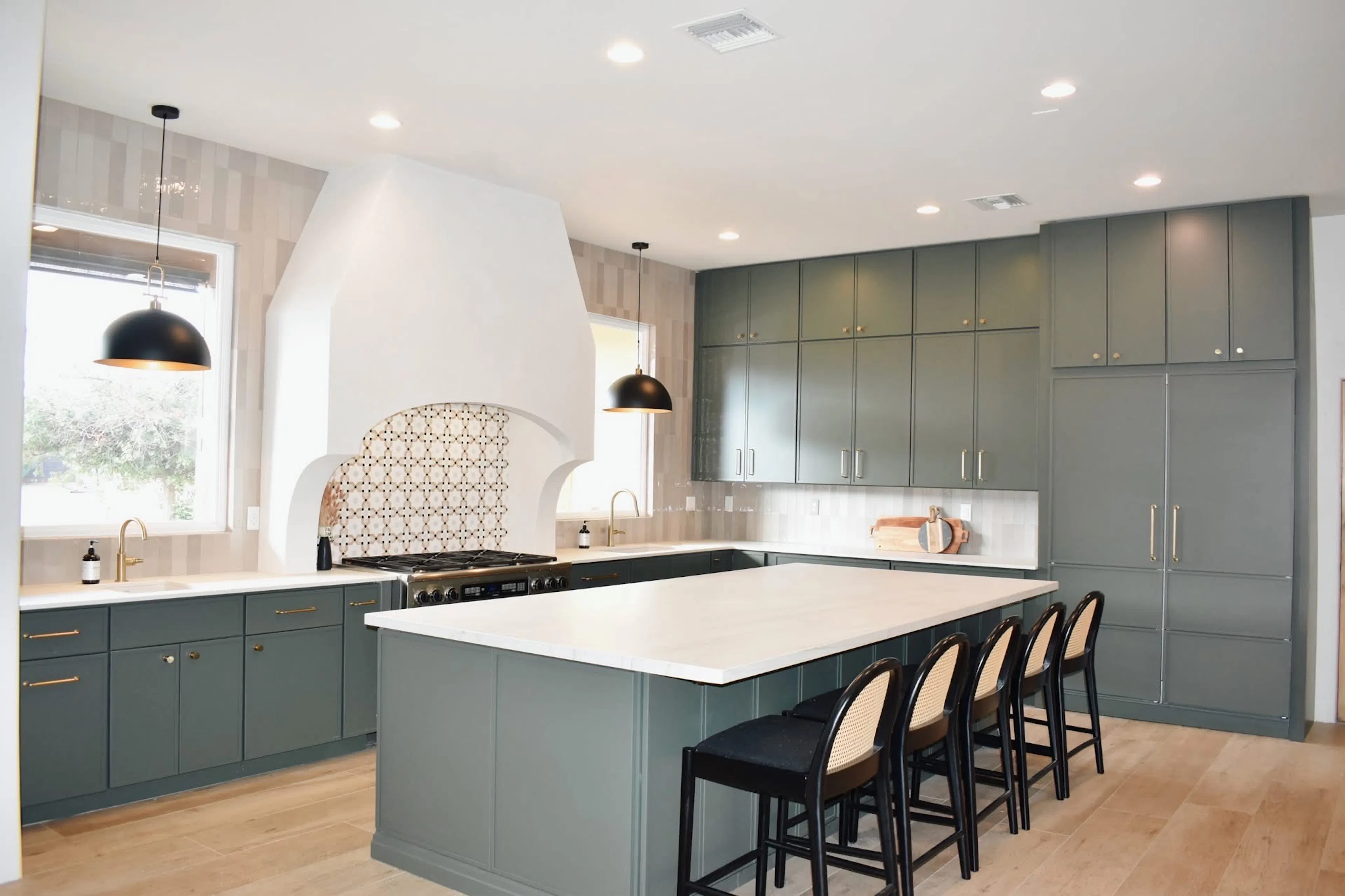 Remodeled kitchen with green cabinetry, a large white island, brass fixtures, and black pendant lights.