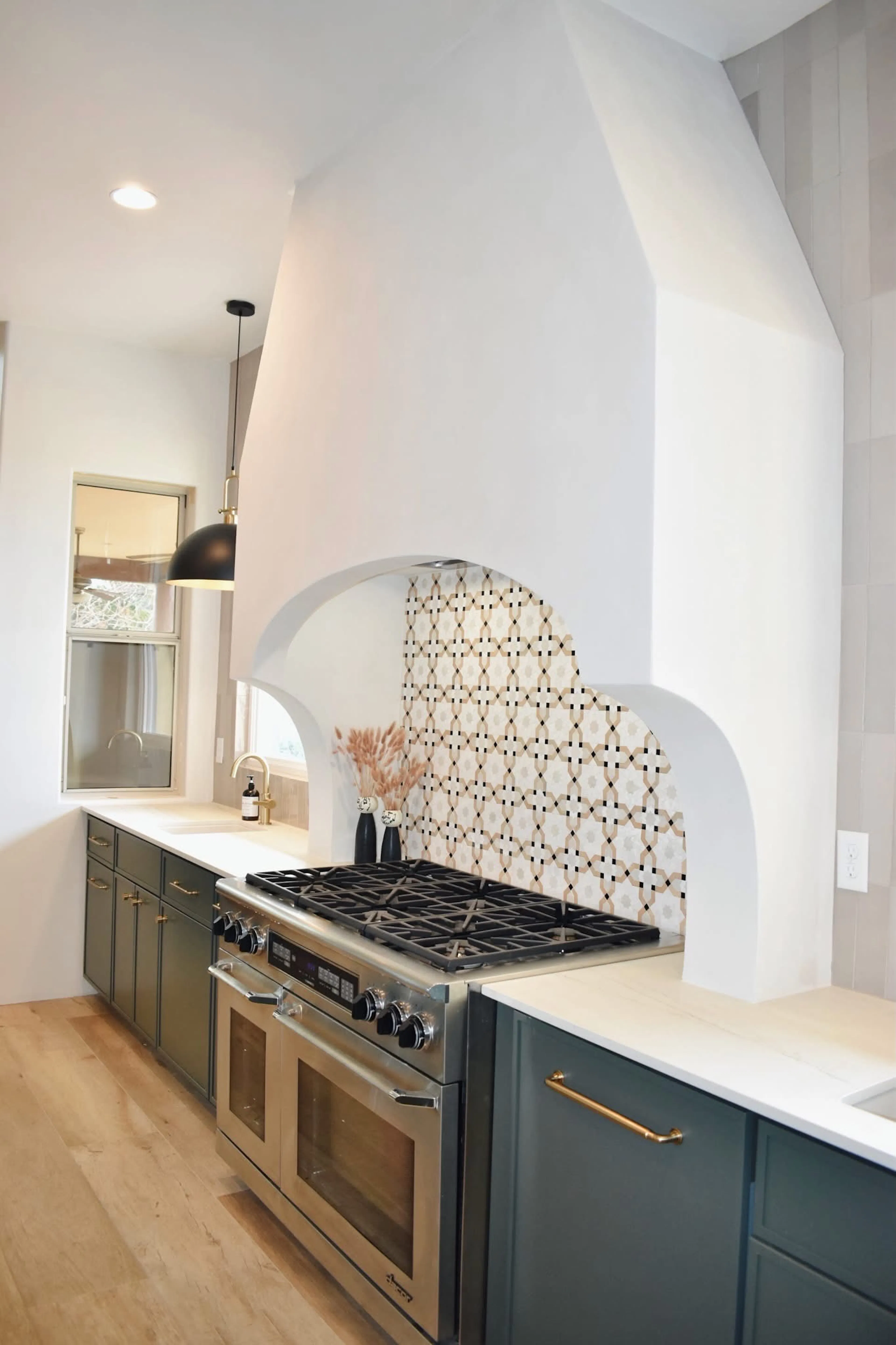 Sculptural plaster range hood with arched patterned-tile inset and green cabinetry.
