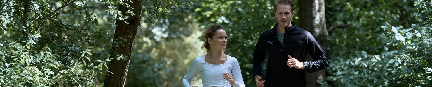 Two smiling adults running through the forest together.