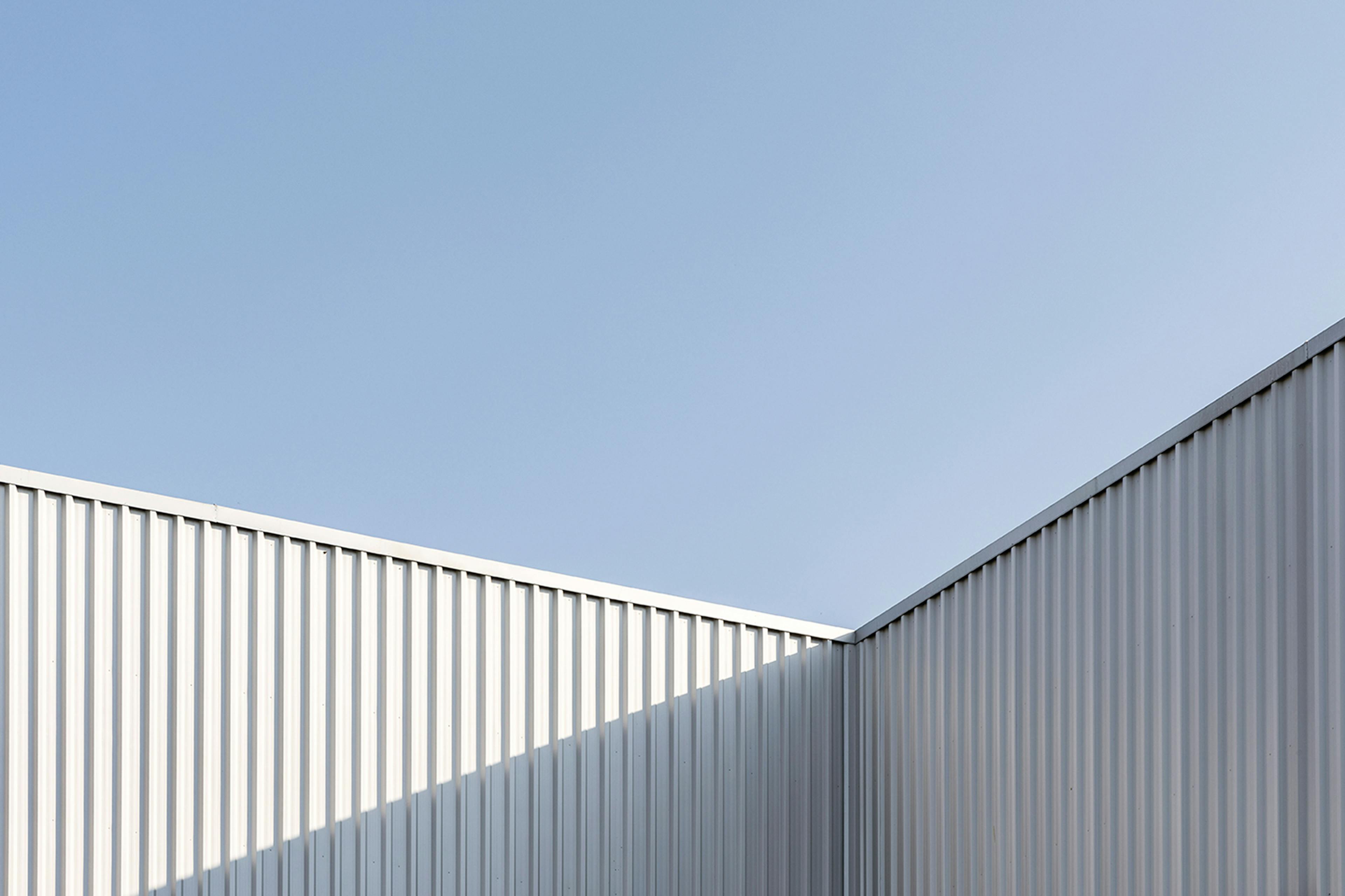 Corrugated metal industrial facade under a clear sky, with shadows and geometric lines