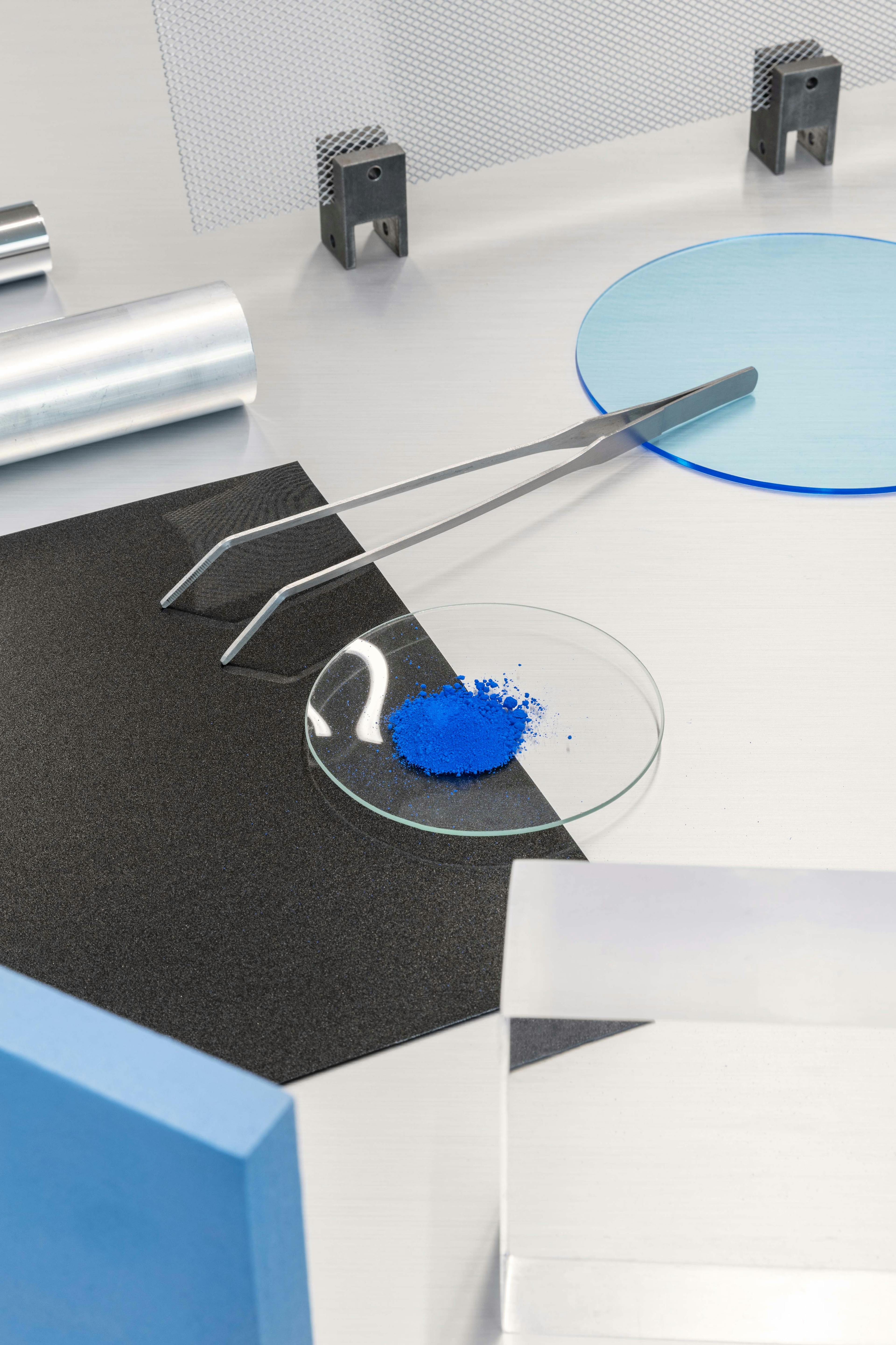 Composition of tech materials on a light background, featuring tweezers and blue powder in a glass dish