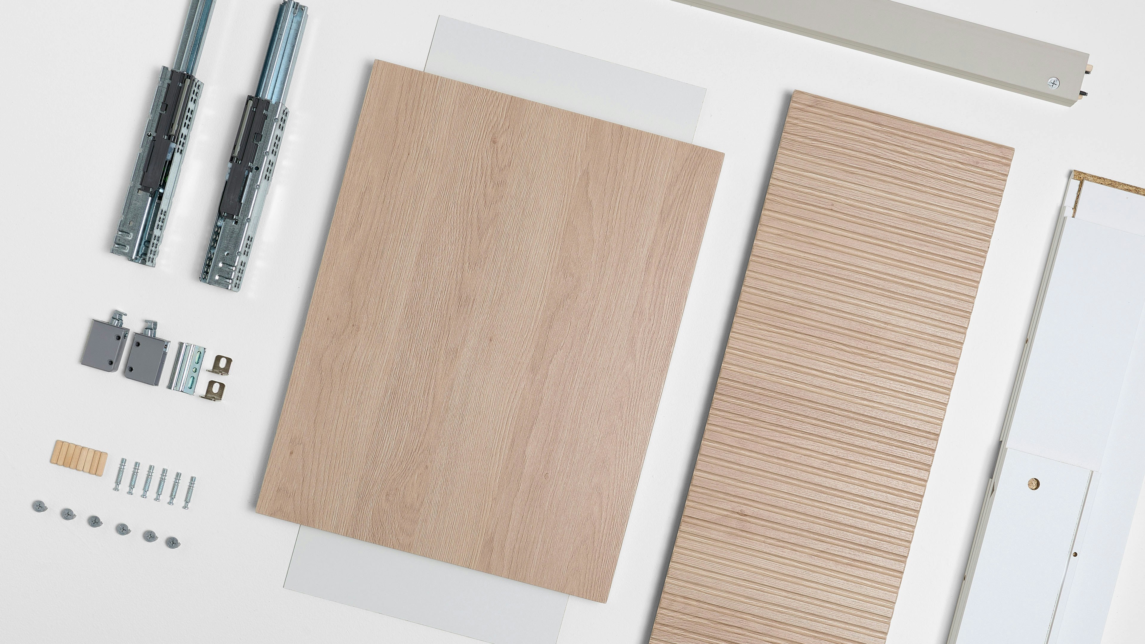 Top-down view of light beige laminate sheets and drawer accessories, featuring subtle wood grain, a linear embossed pattern on one of the sheets, and gray metallic components.