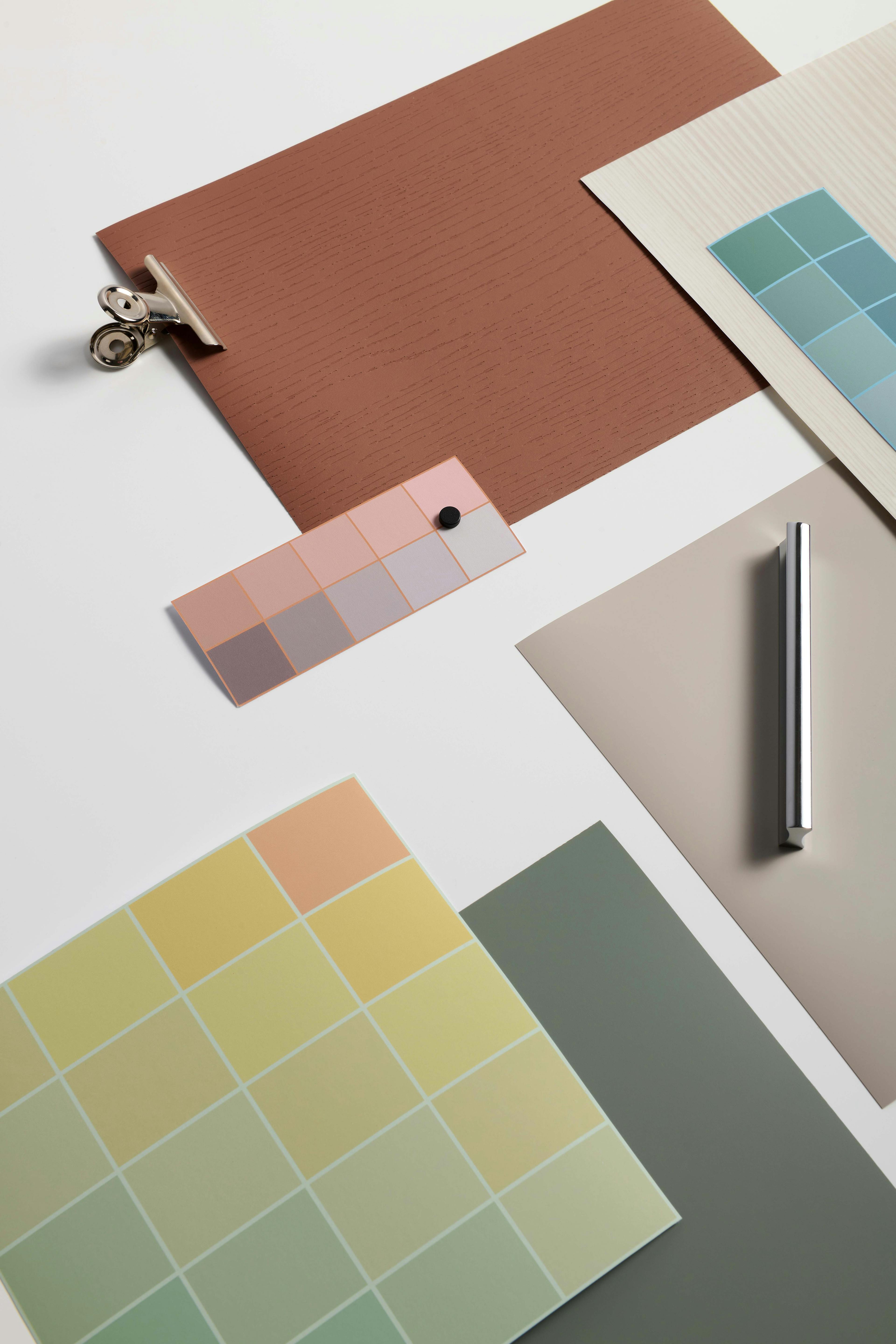 Un'immagine di tonalità di colori, disposte su fogli di carta, in un'ampia varietà di sfumature, dai caldi aranci ai grigi pastello.