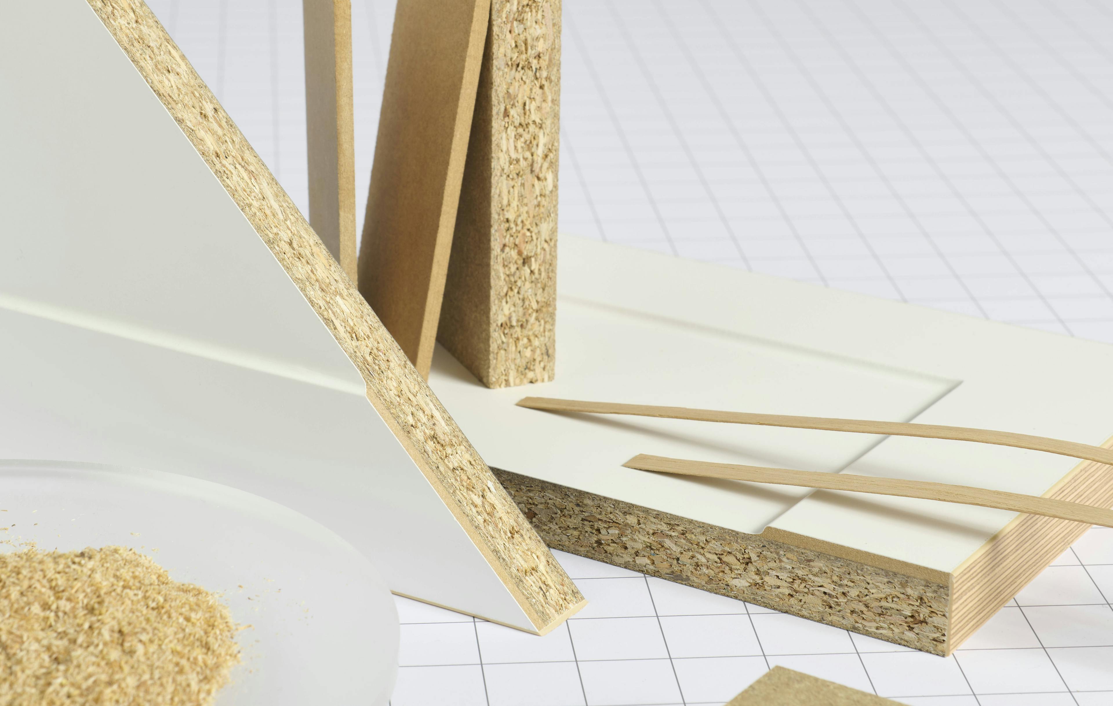 Pieces of particleboard and plywood in various shapes and sizes, light beige and off-white.  Different layers of the wood are visible, showing the wood fibers and grains. 