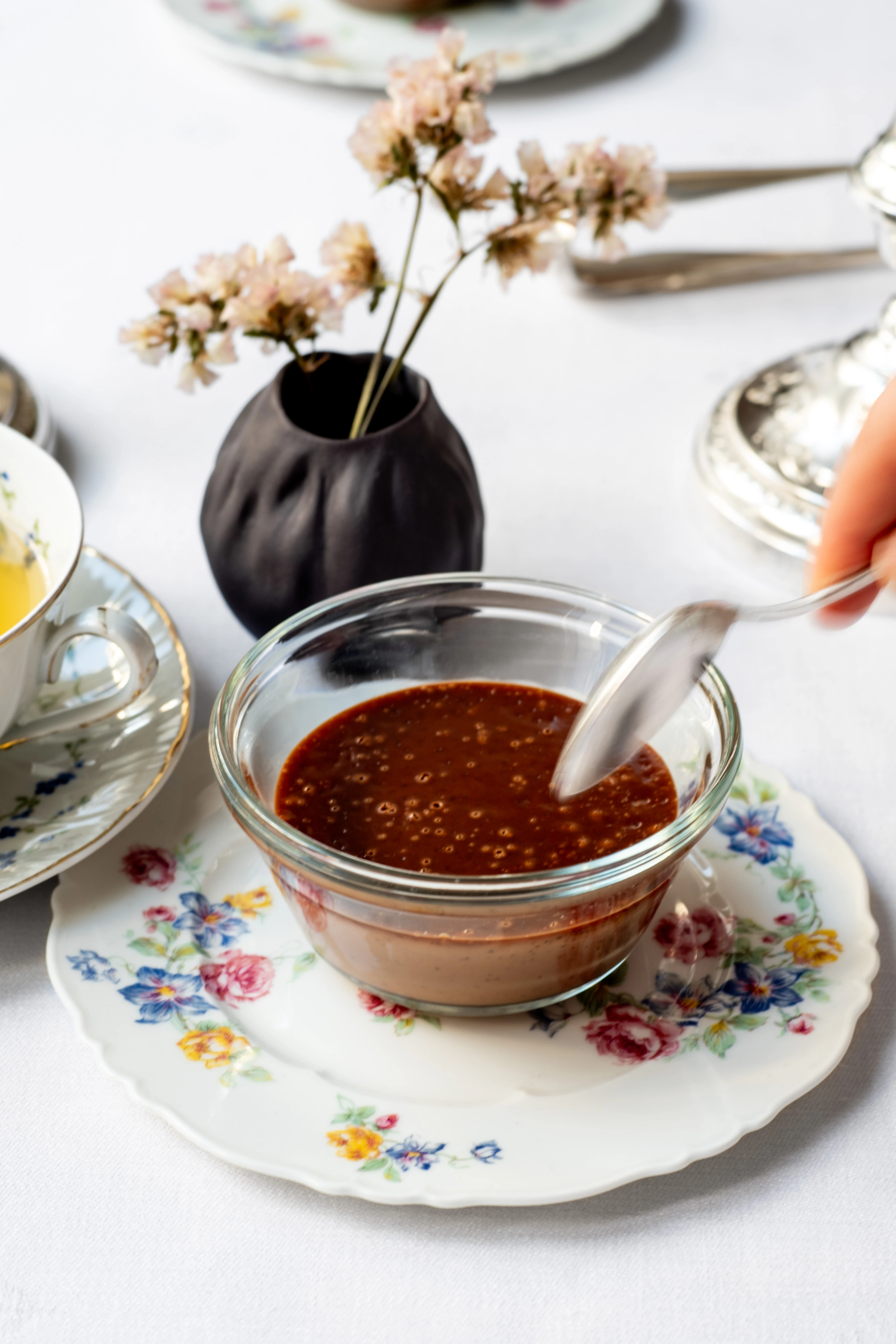 A spoon reaches for a chocolate cream dessert. The dessert sits on a floral-print plate.