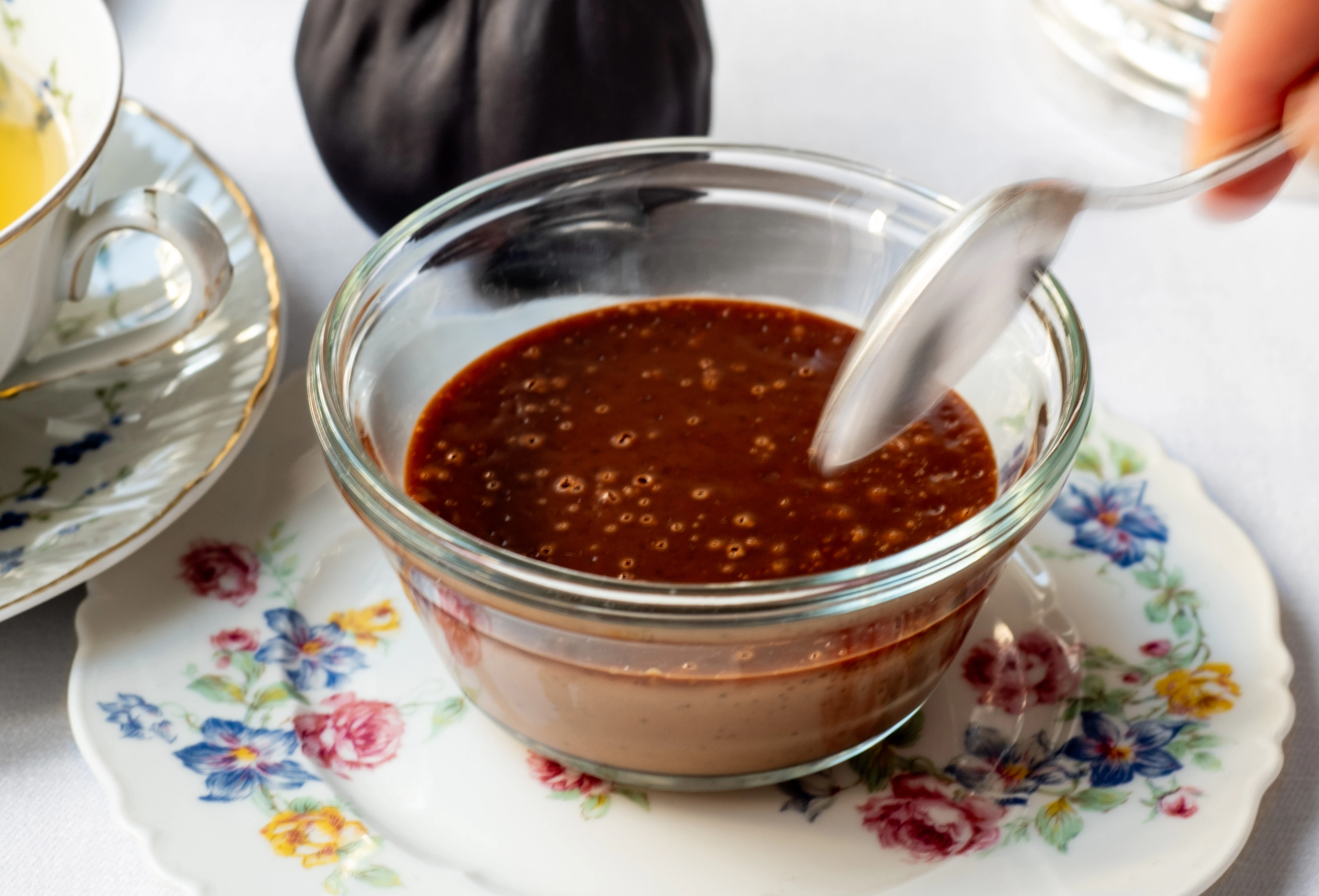 A spoon reaches for a chocolate cream dessert. The dessert sits on a floral-print plate.