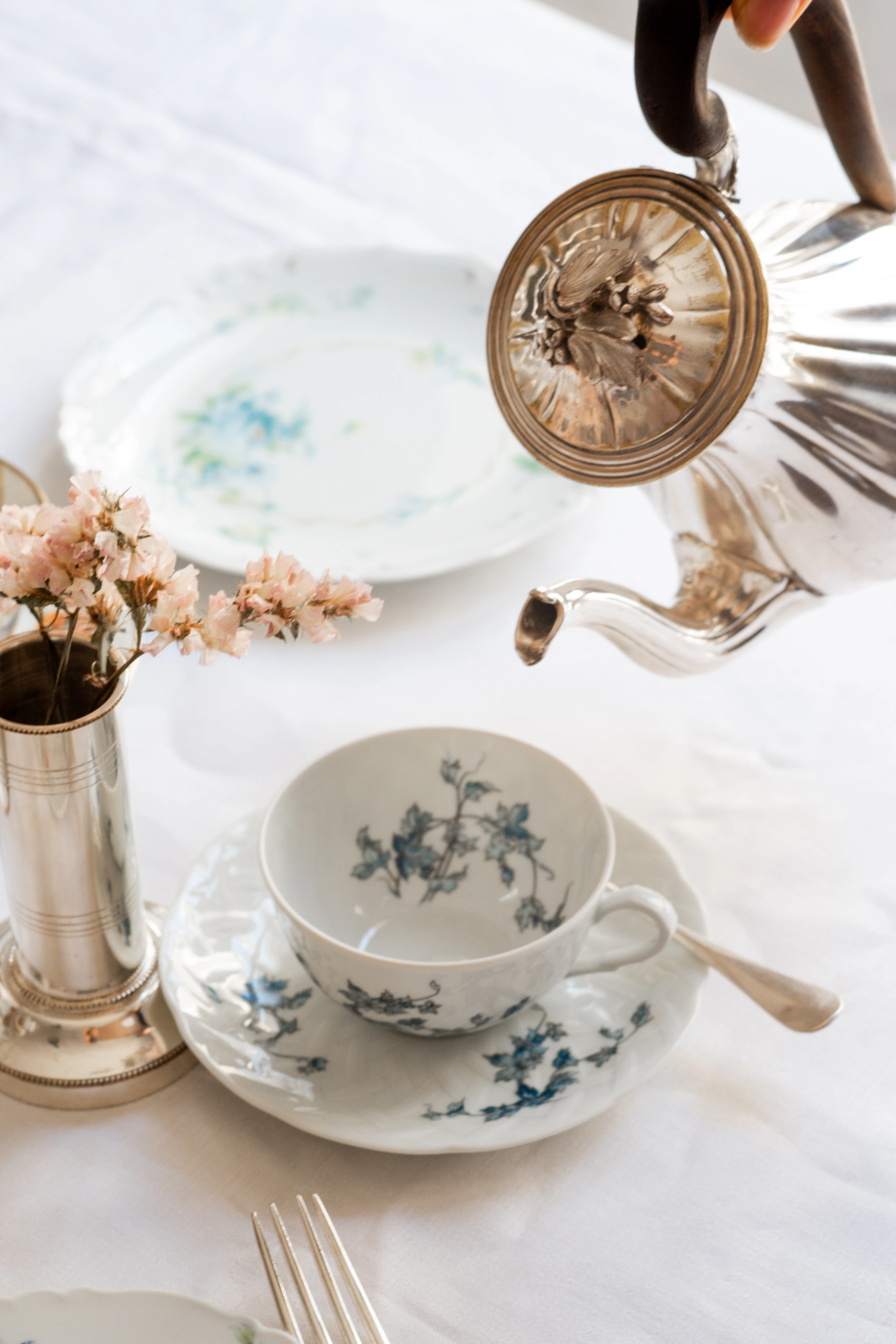 A silver tea pot and a white teacup and saucer with blue floral print.