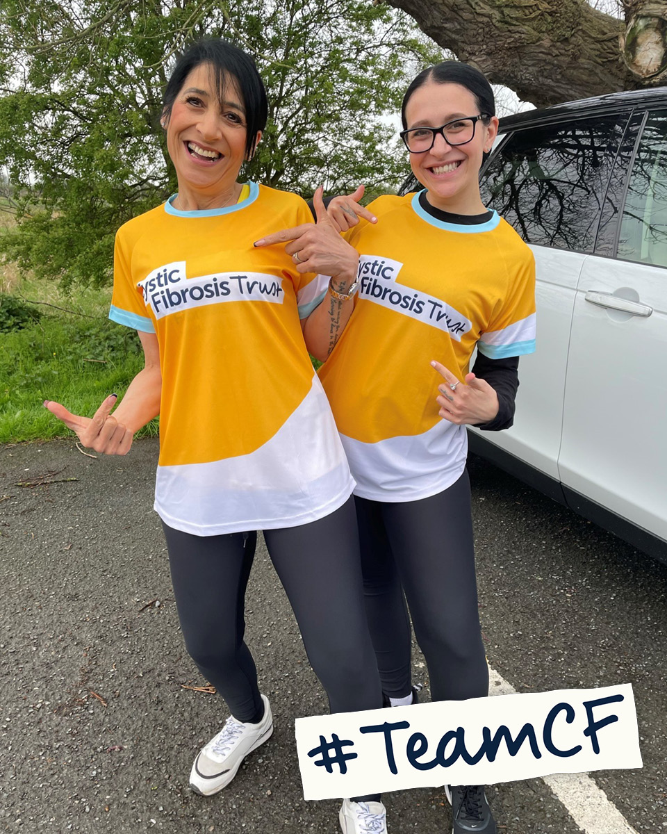 Two smiling people pointing at their yellow Cystic Fibrosis Trust t-shirts