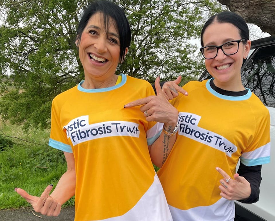 Two smiling people pointing at their yellow Cystic Fibrosis Trust t-shirts
