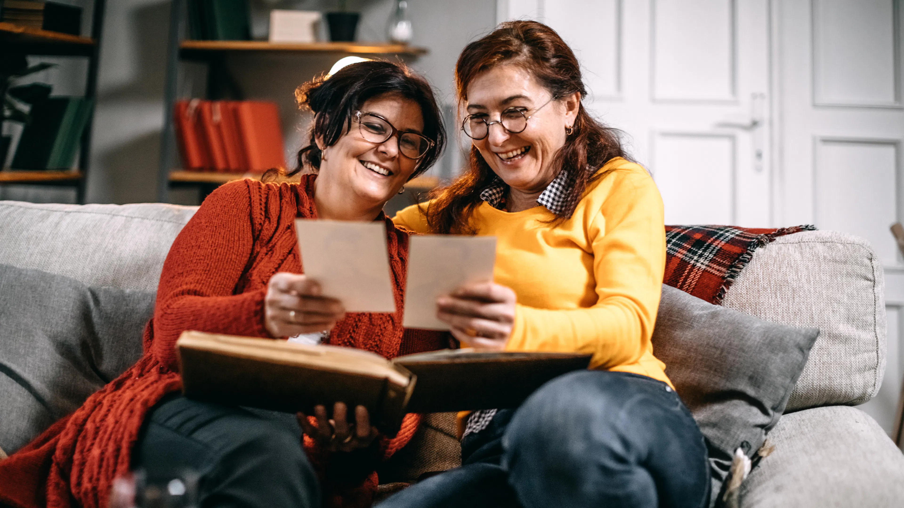 Two women on a sofa smiling at photos and memories