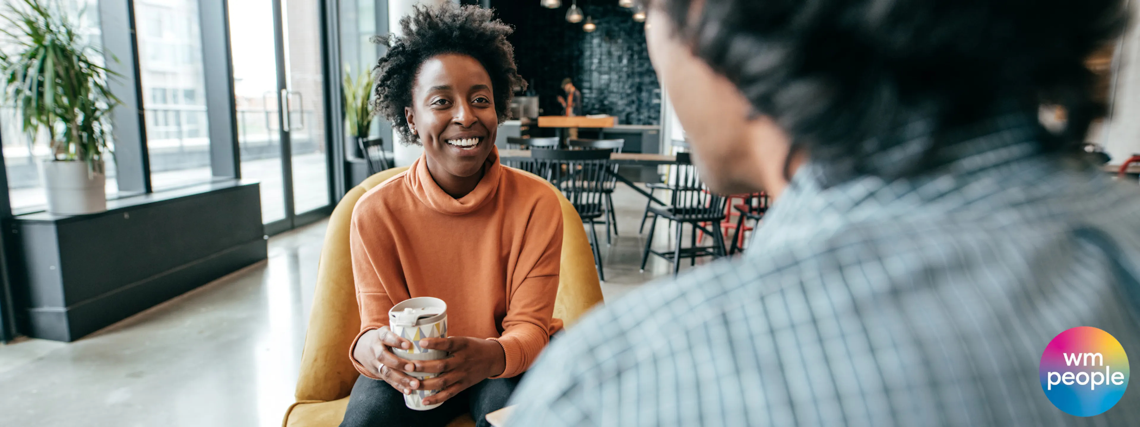 Black female worker holding coffee mentoring male colleague with back to camera