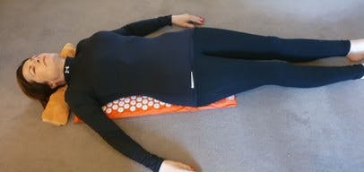 Hilda Smith lying down on a red shakti mat with white spikes with a towel under her neck