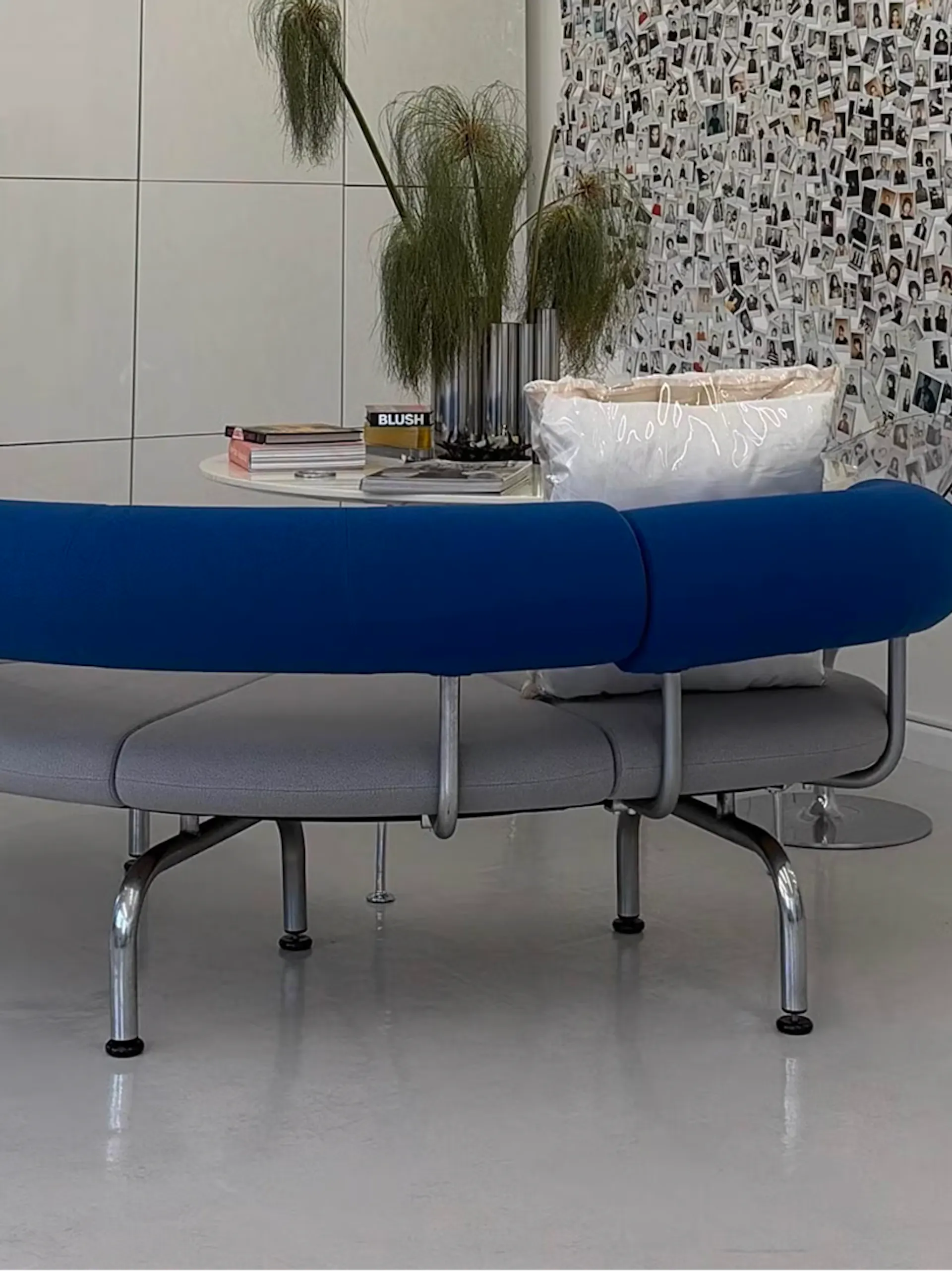 Curved blue bench in front of a wall of polaroid photos
