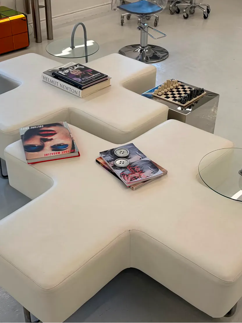 Cross-shaped white leather lounge with fashion books and a chess set in the waiting area