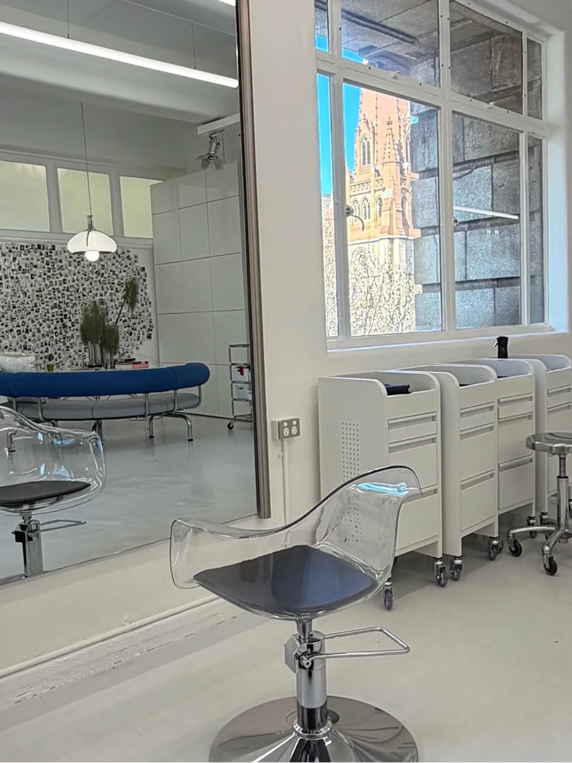 Clear acrylic salon chair and white trolleys by a window with a view of a cathedral spire