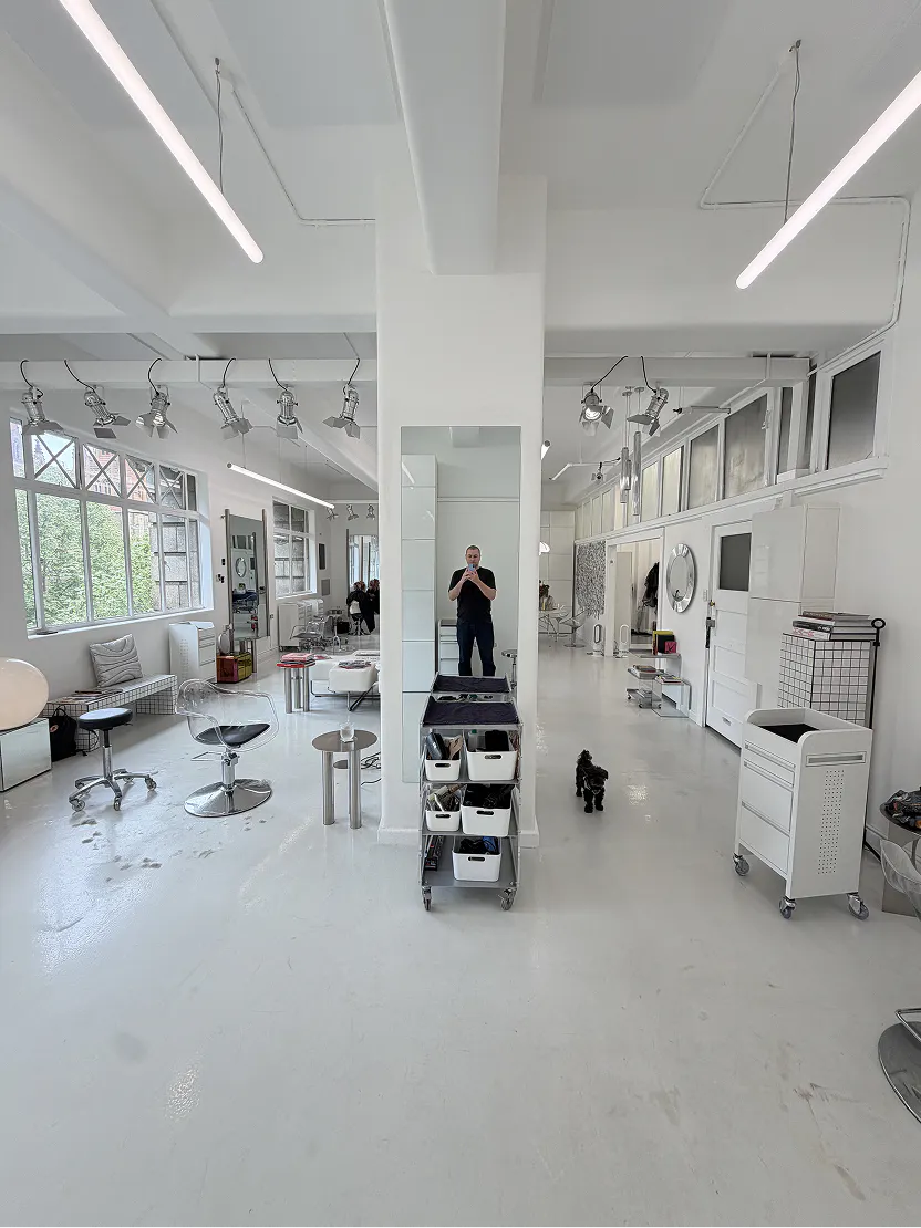 Open-plan white salon floor with styling chairs, trolleys and large windows