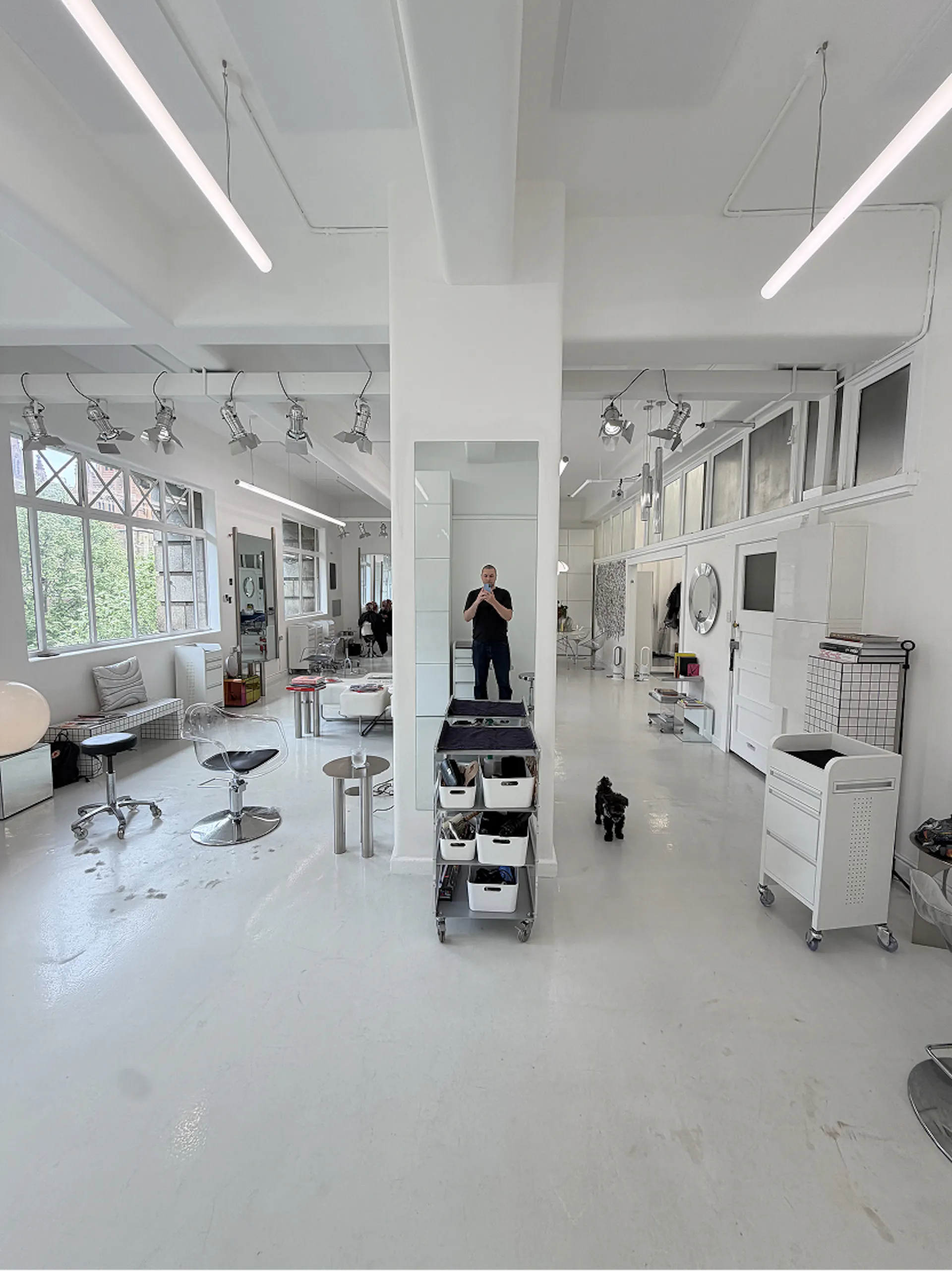 Open-plan white salon floor with styling chairs, trolleys and large windows