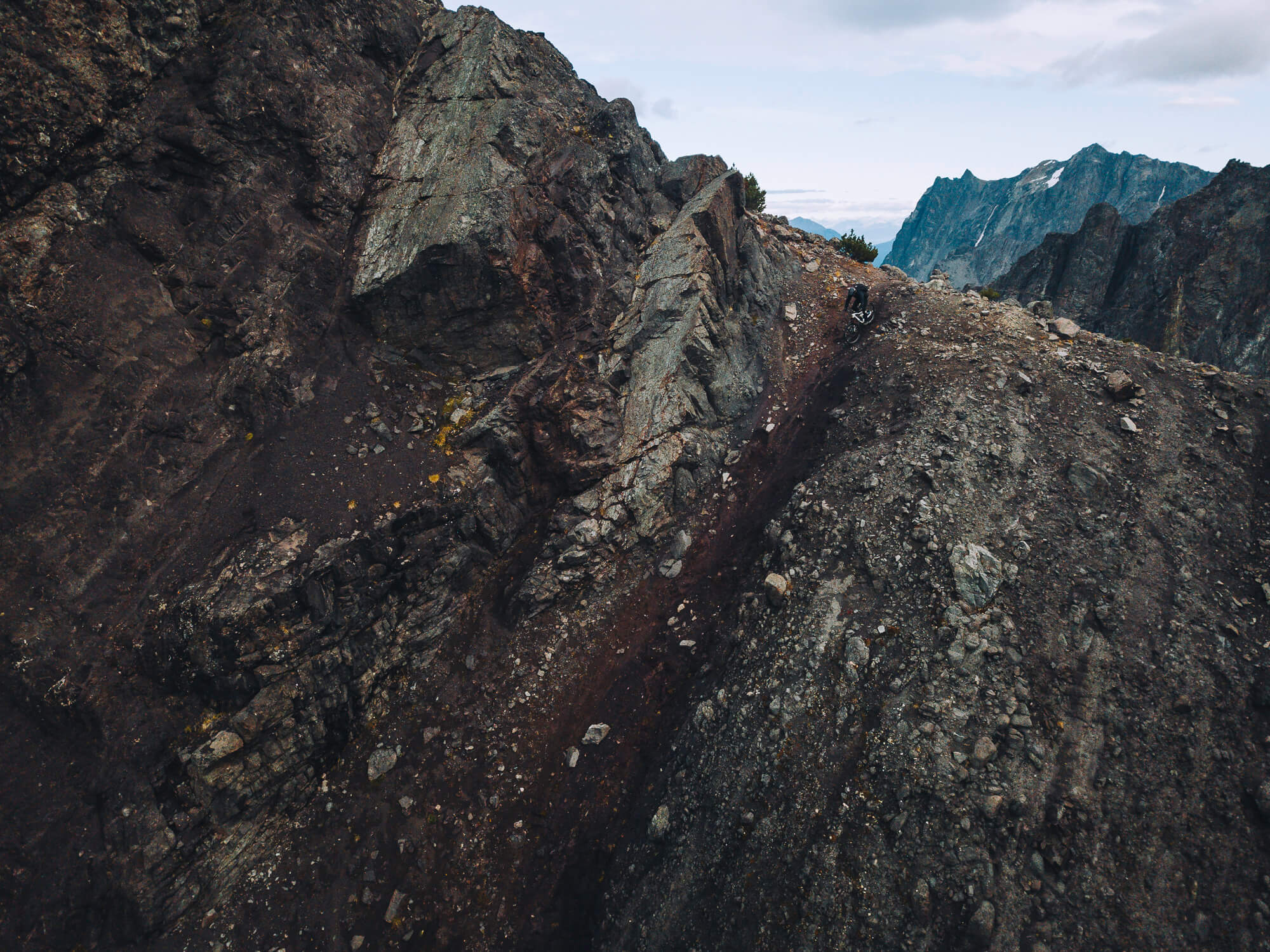 Aerial view of a lone rider on a narrow rocky ridge spine