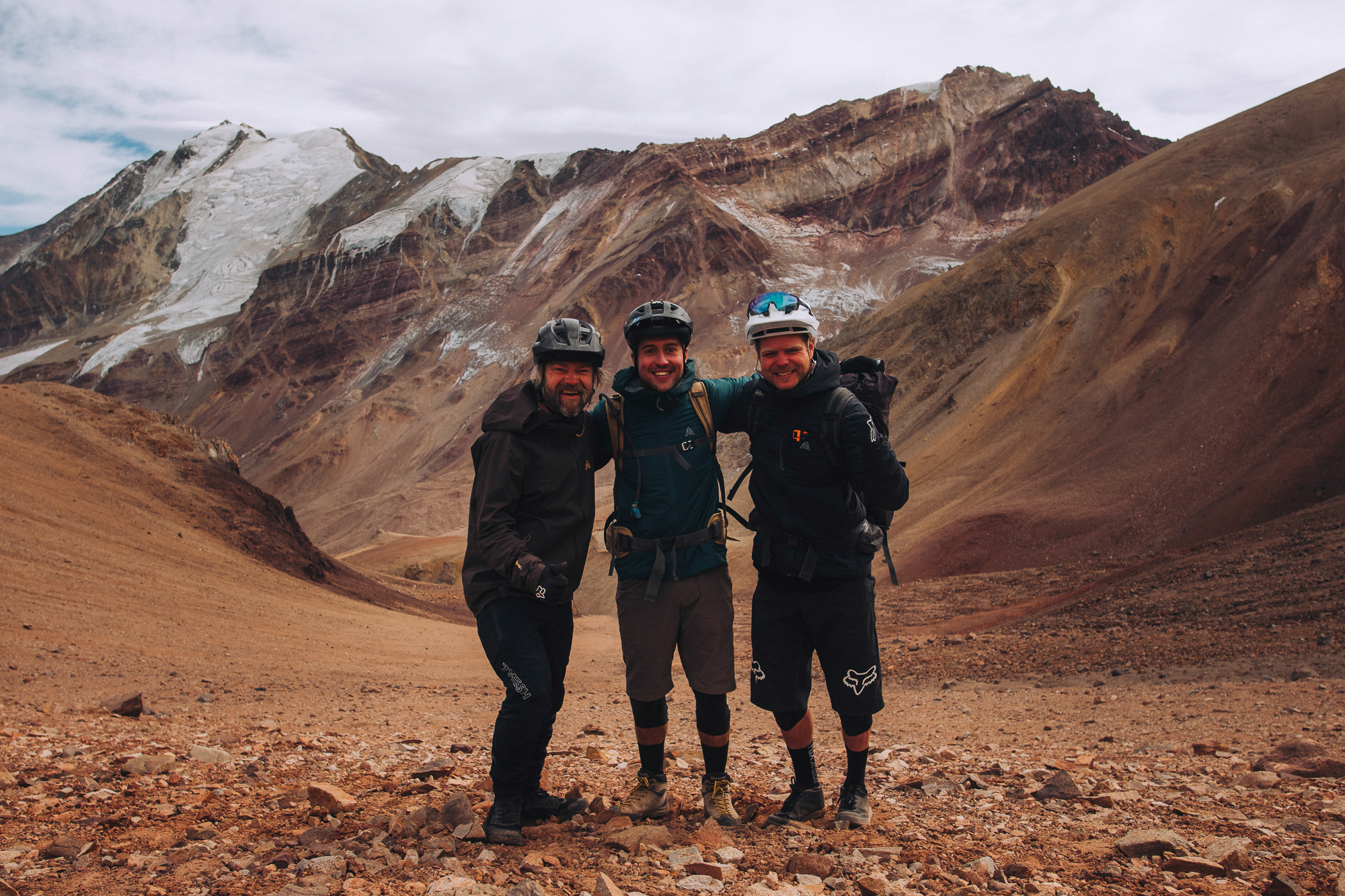 Three riders standing together for a group photo below a glaciated peak